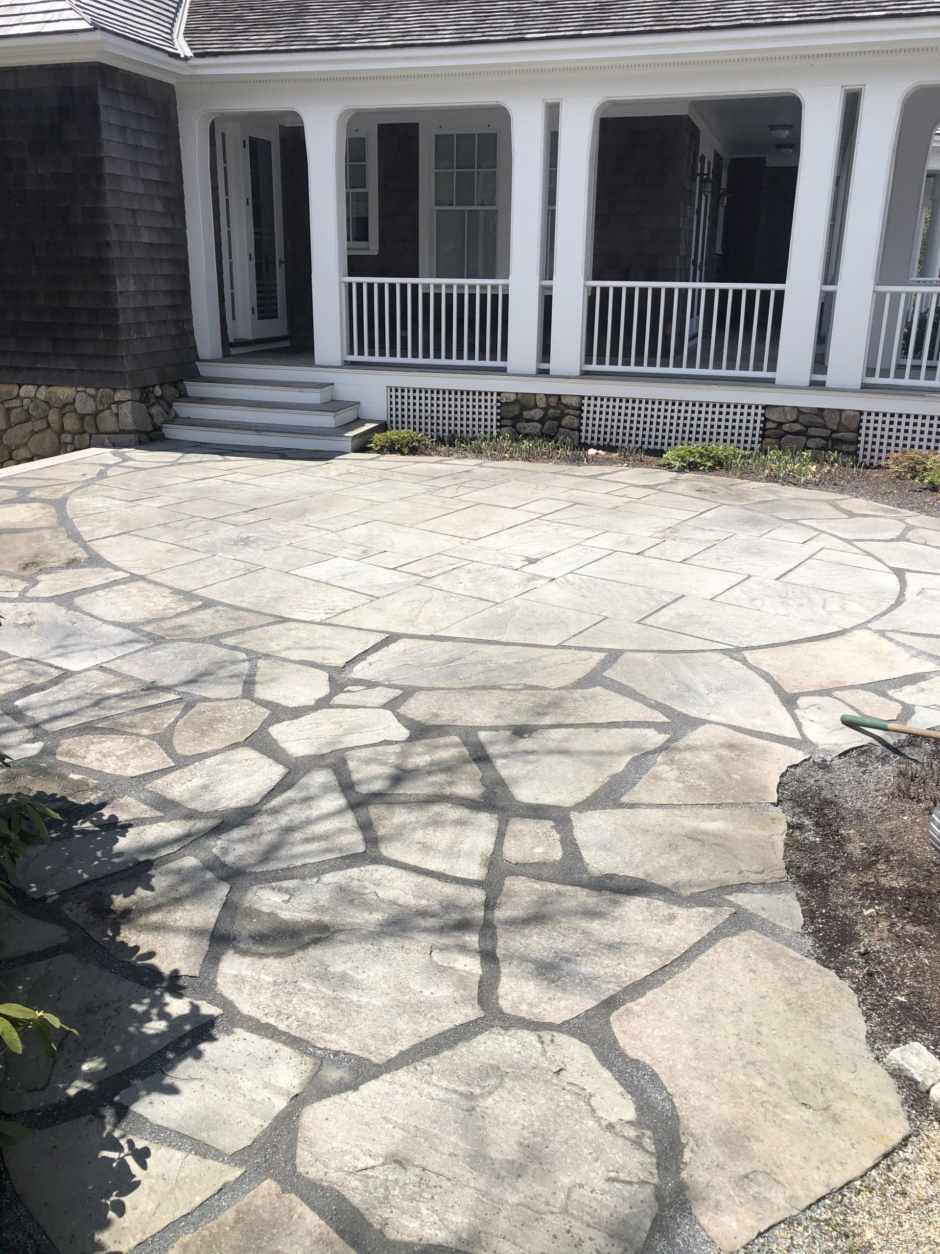 A stone patio in front of a house with a porch.