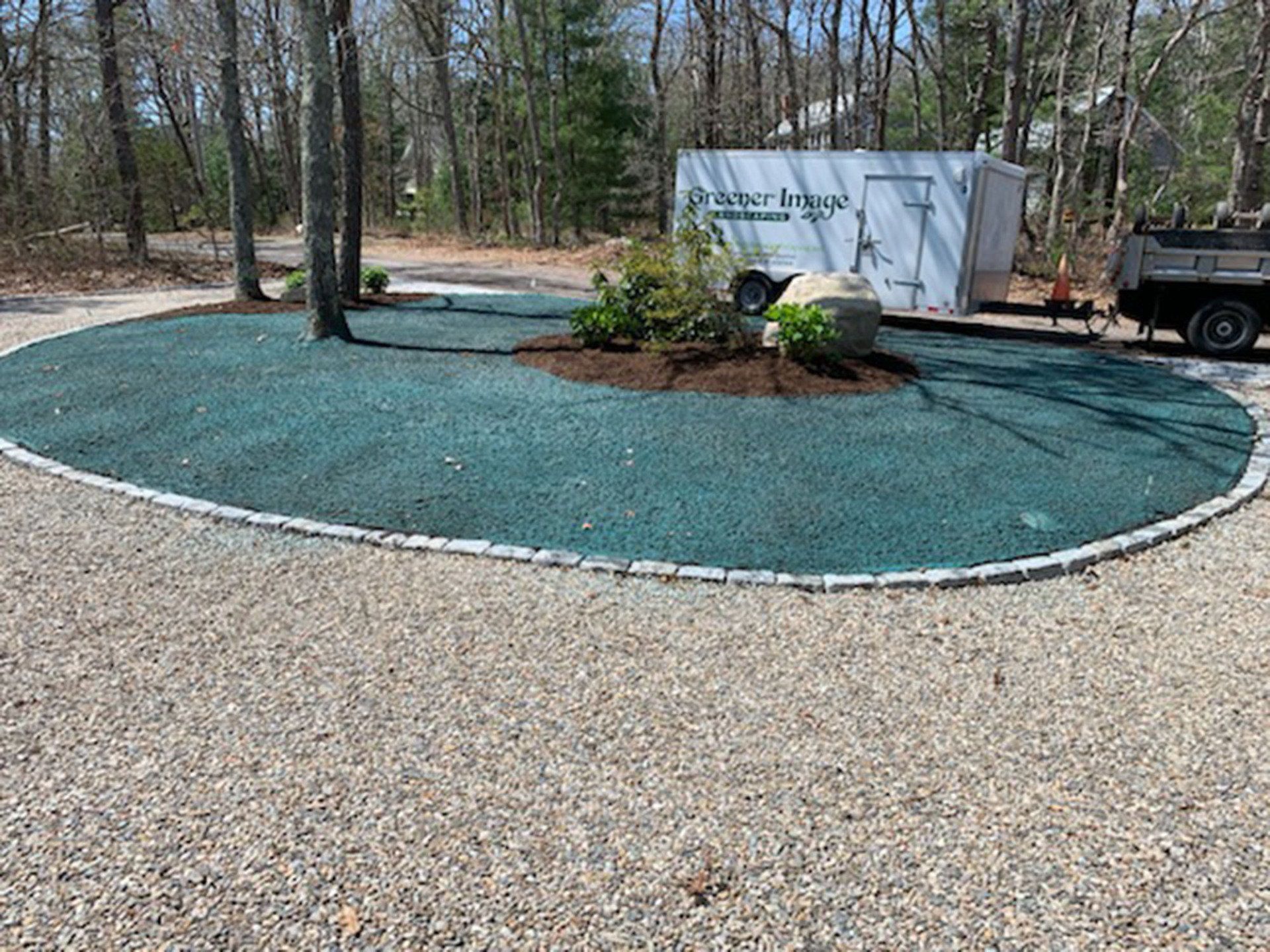 A truck is parked in a gravel driveway next to a circle of green mulch