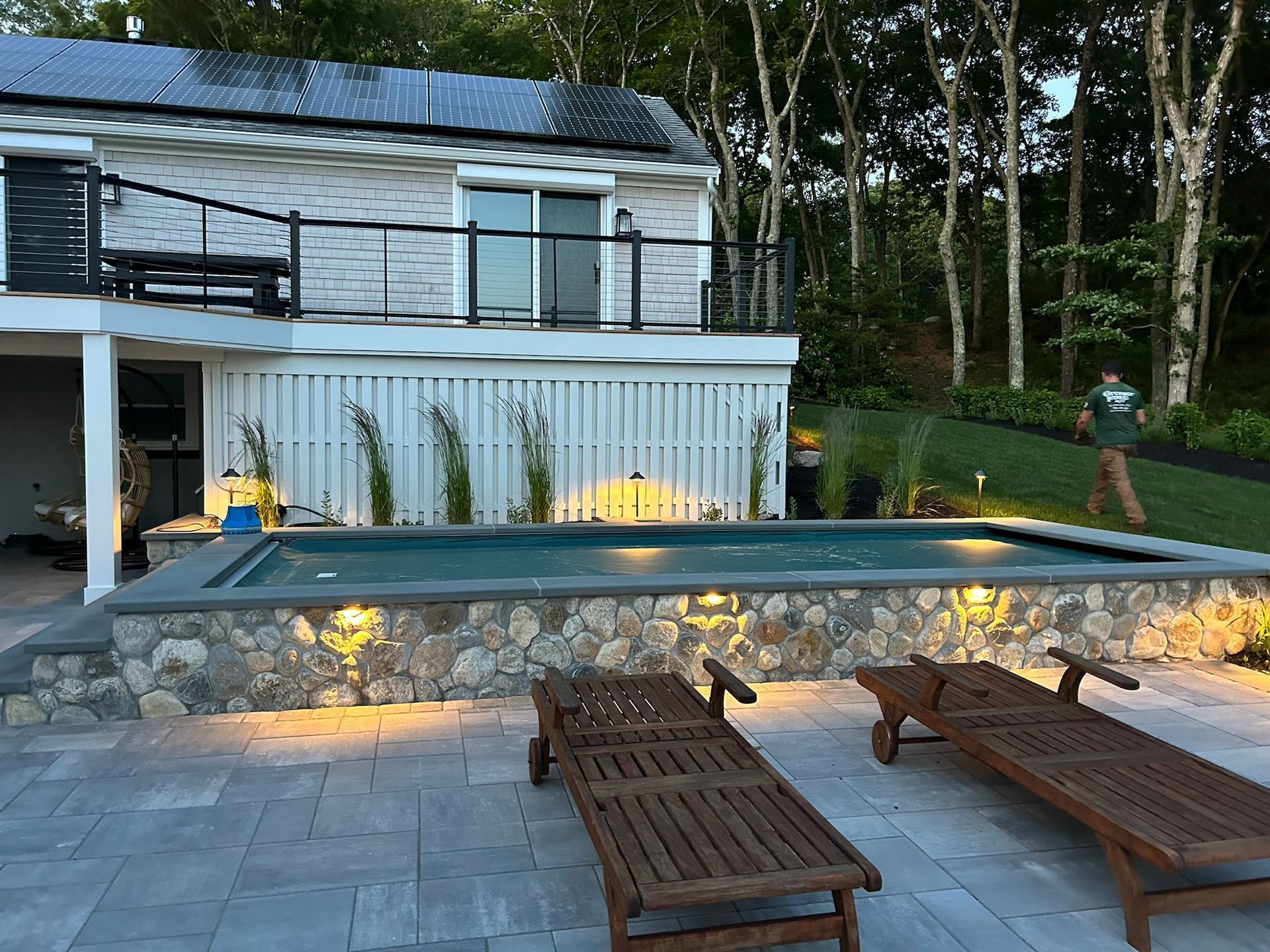 A large swimming pool is surrounded by lawn chairs and a house with solar panels on the roof