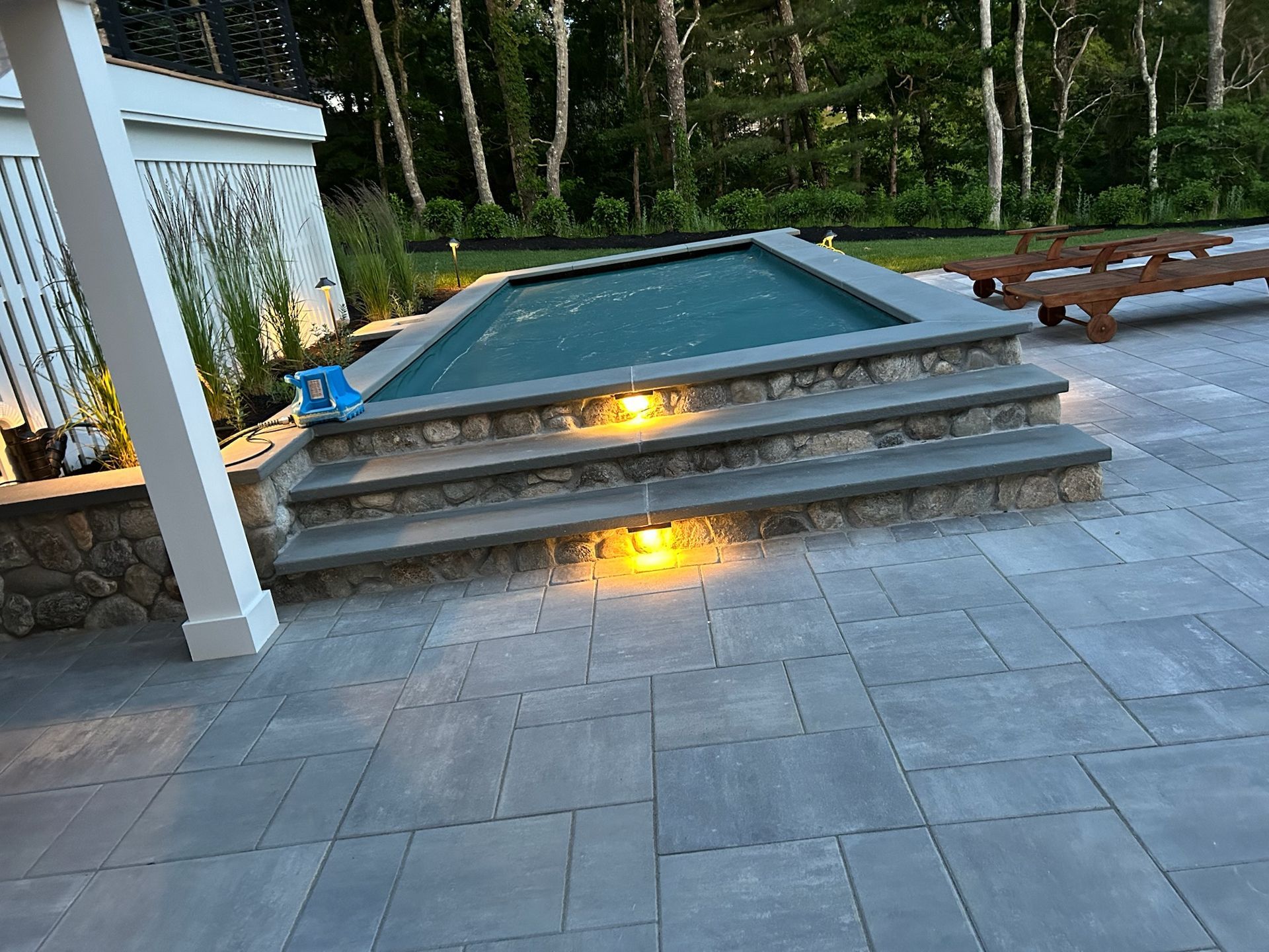A patio with stairs leading up to a pool and trees in the background