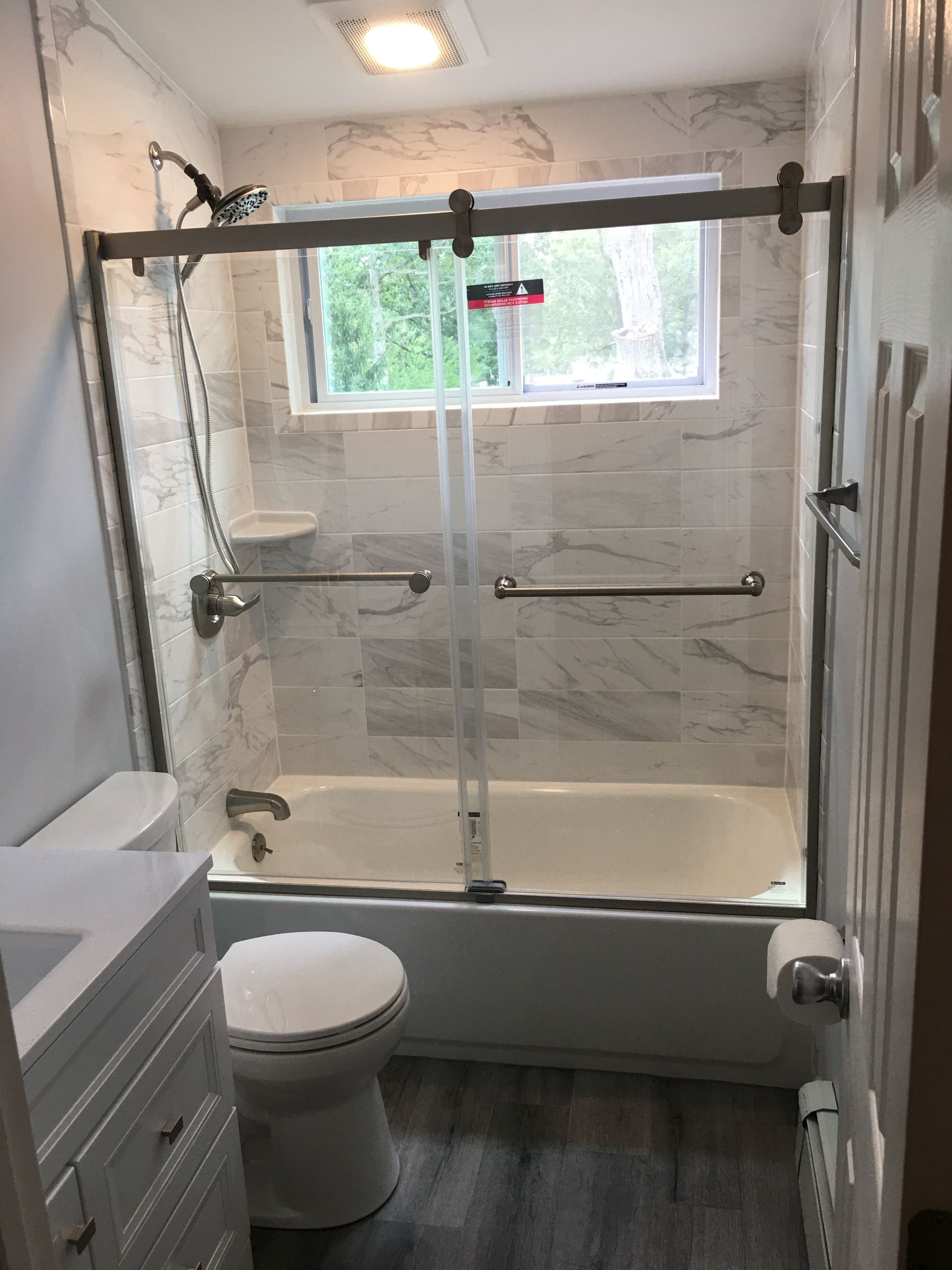 Bathroom with a tub, sliding glass shower door, and marble look tile. Toilet and vanity are visible.