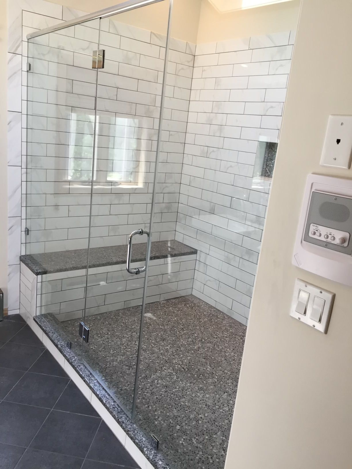 A bathroom with a walk in shower with a glass door and a bench