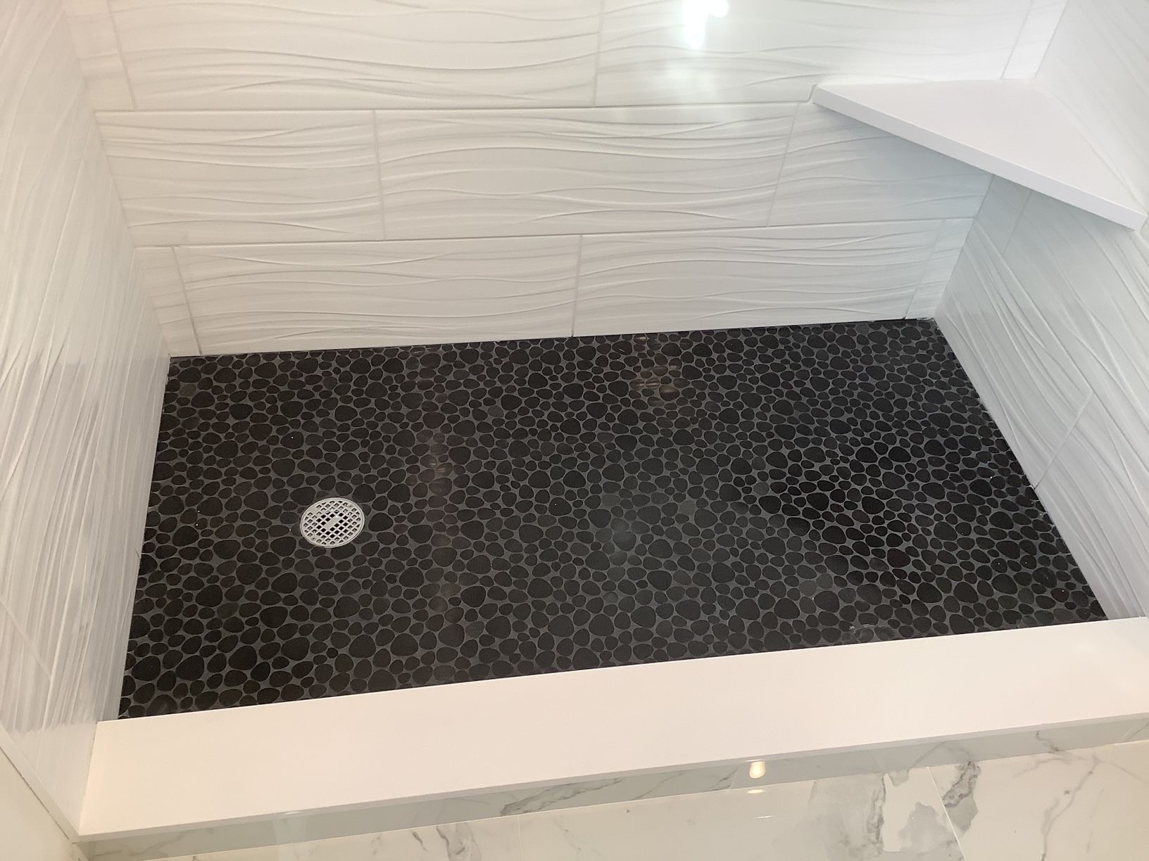 A shower stall with a black tile floor and a drain