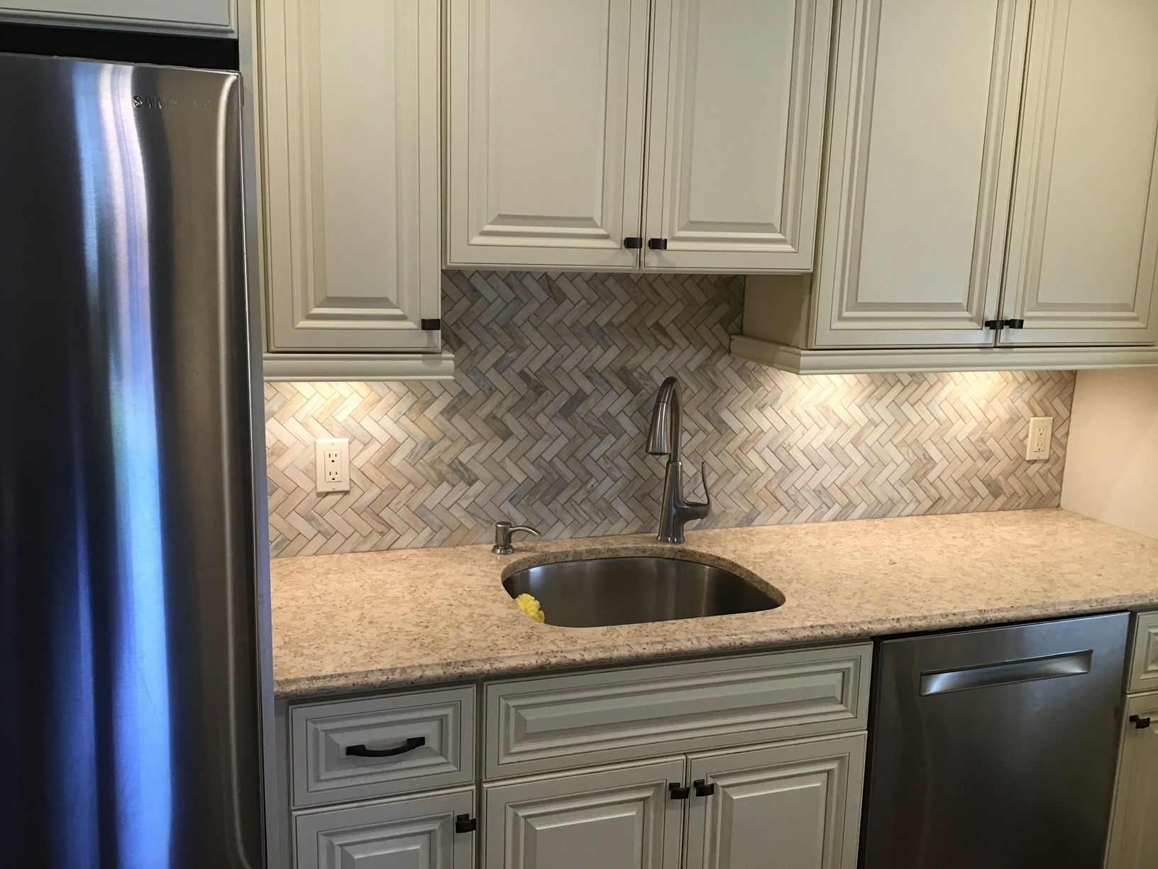 A kitchen with white cabinets, a stainless steel refrigerator, a sink, and a dishwasher