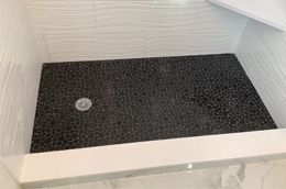 A shower stall with a black tile floor in a bathroom