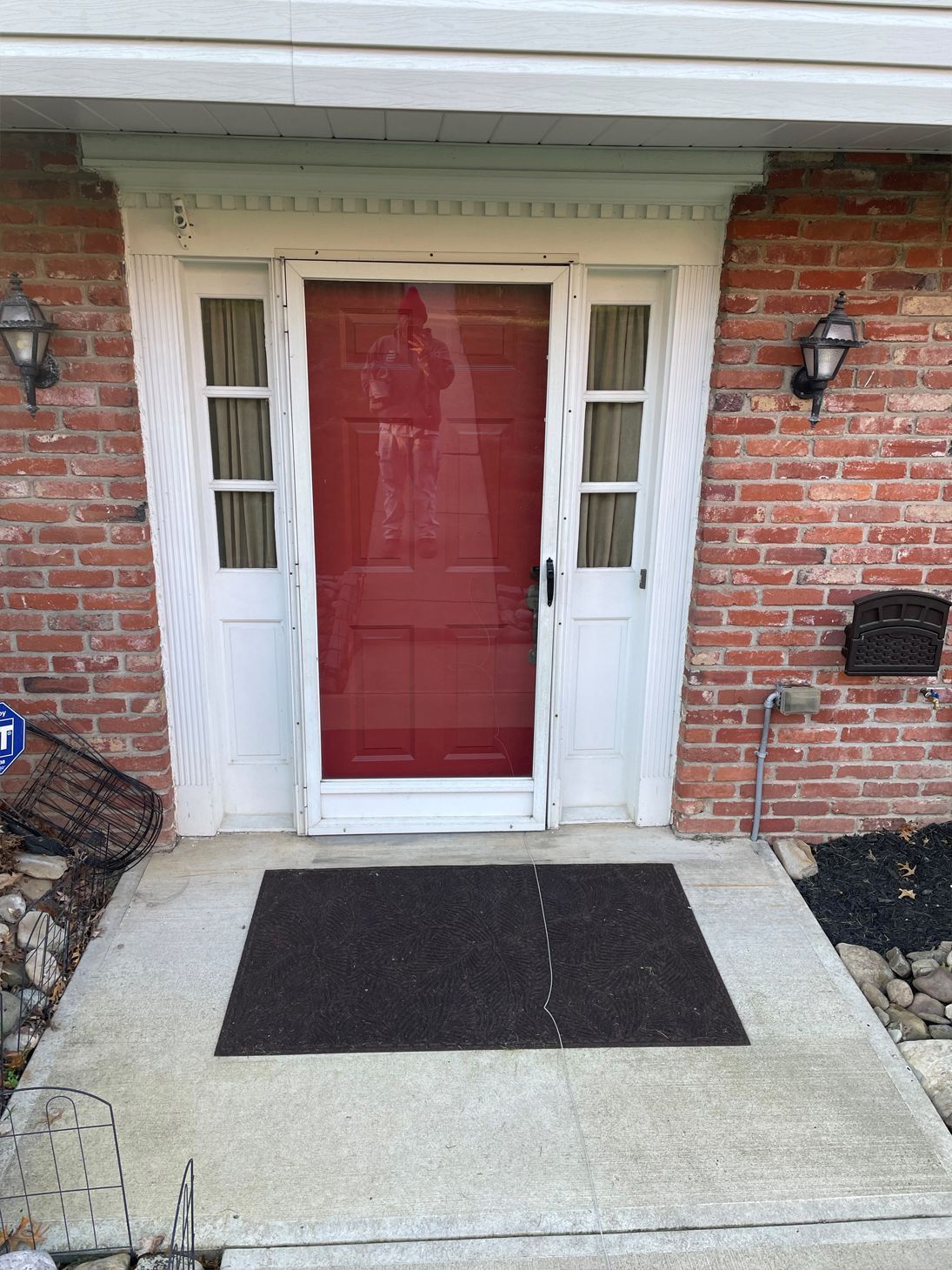 The front door of a brick house with a red door and a brown mat.