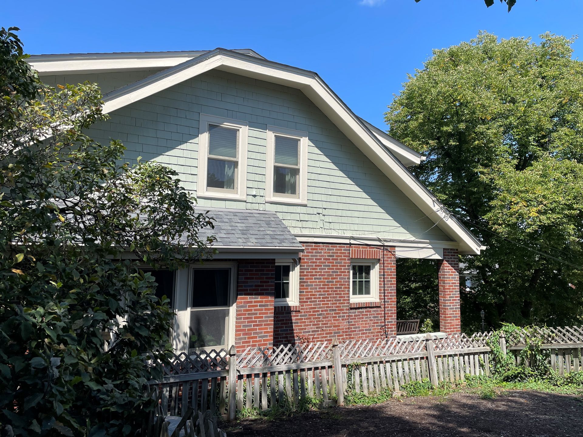 A brick house with a green siding and a white roof