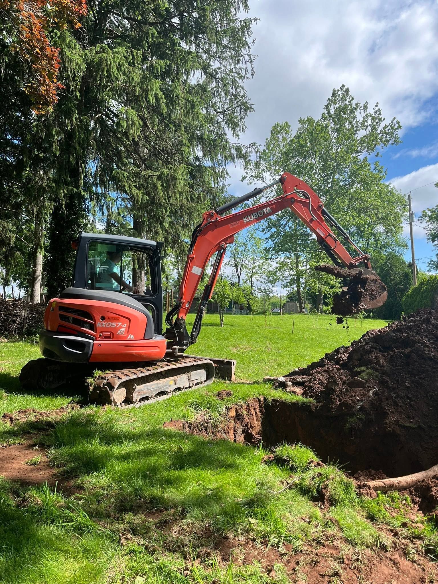 Orange excavator digging a trench on a grassy hillside under trees and blue sky