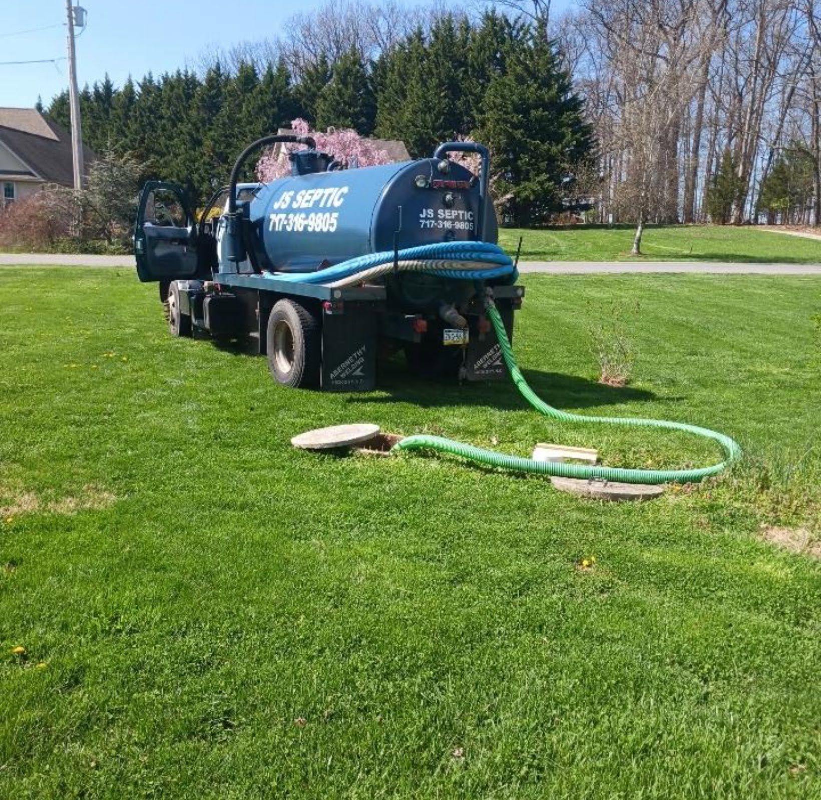 Blue septic service truck on a grassy lawn with hoses laid out in a suburban yard.