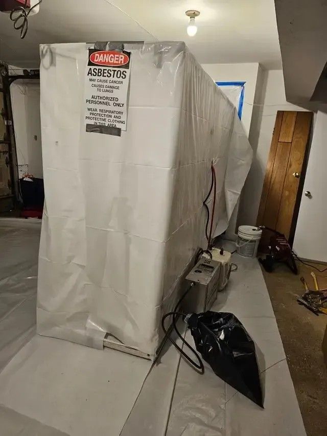 Asbestos abatement enclosure in a basement, wrapped in white plastic with a warning sign.