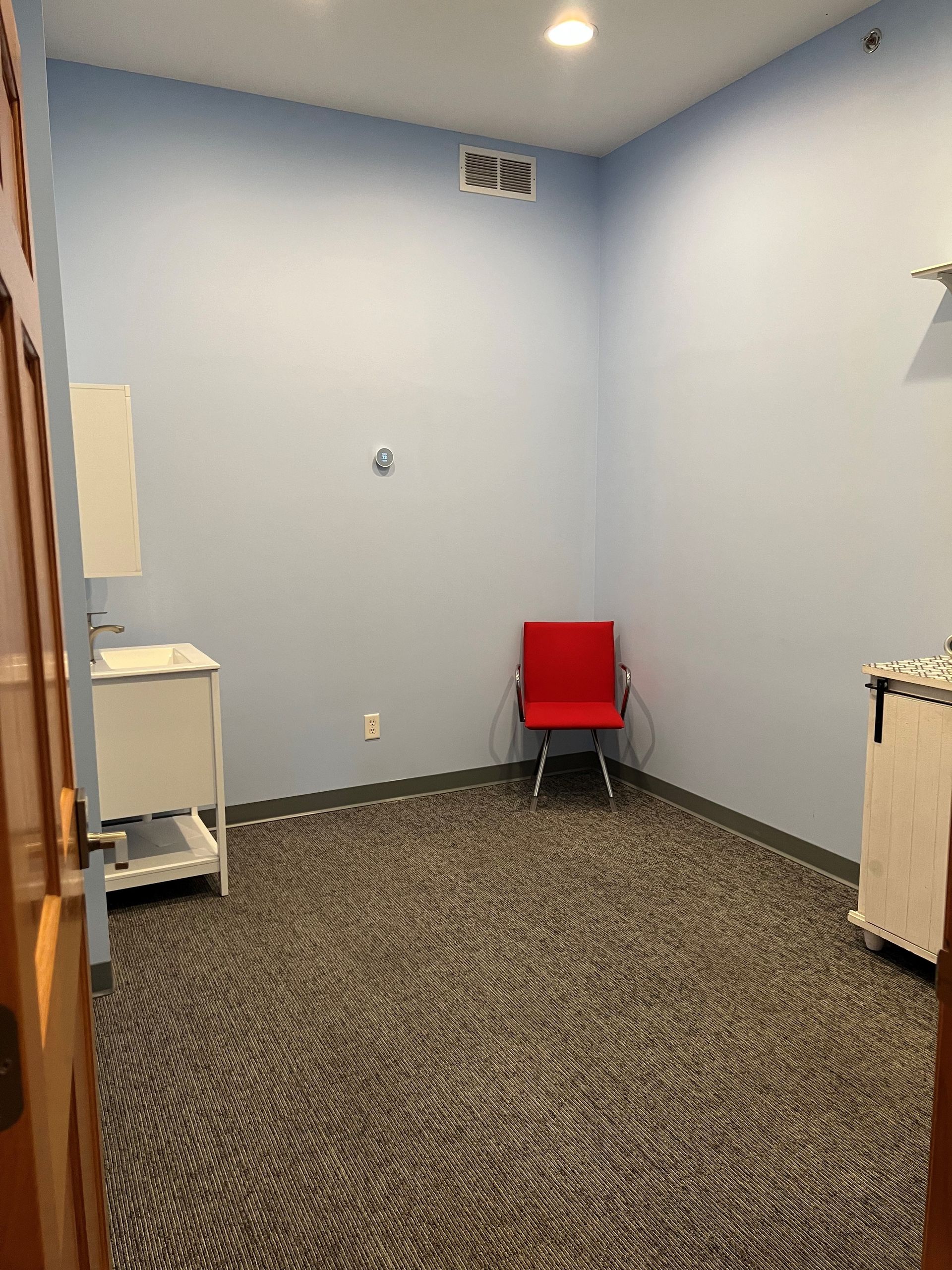 Small room with blue walls, patterned carpet, a red chair, a sink, and a cabinet.