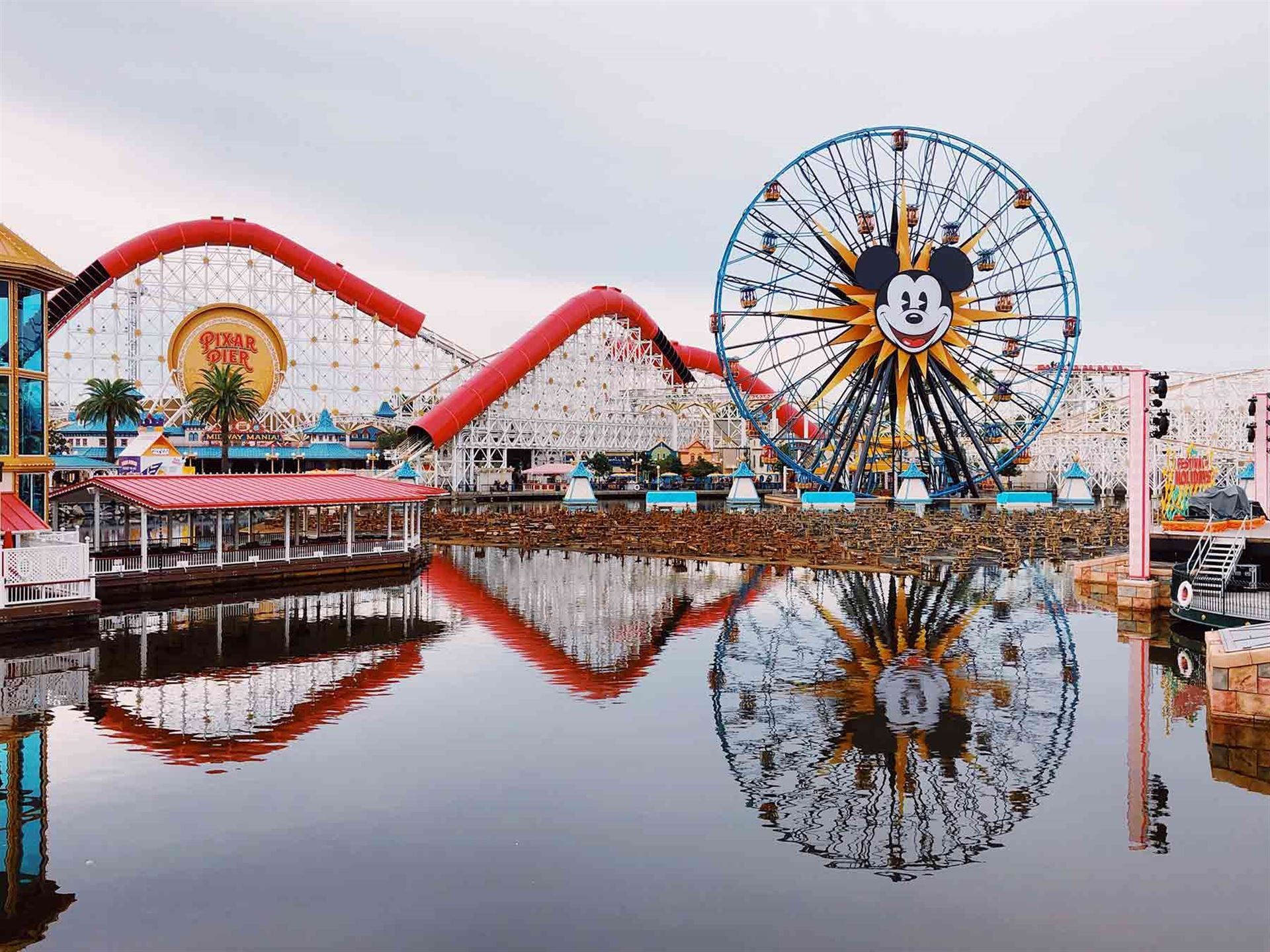 A roller coaster and ferris wheel are reflected in the water at an amusement park.