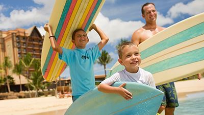 A man and two children are holding surfboards on the beach.