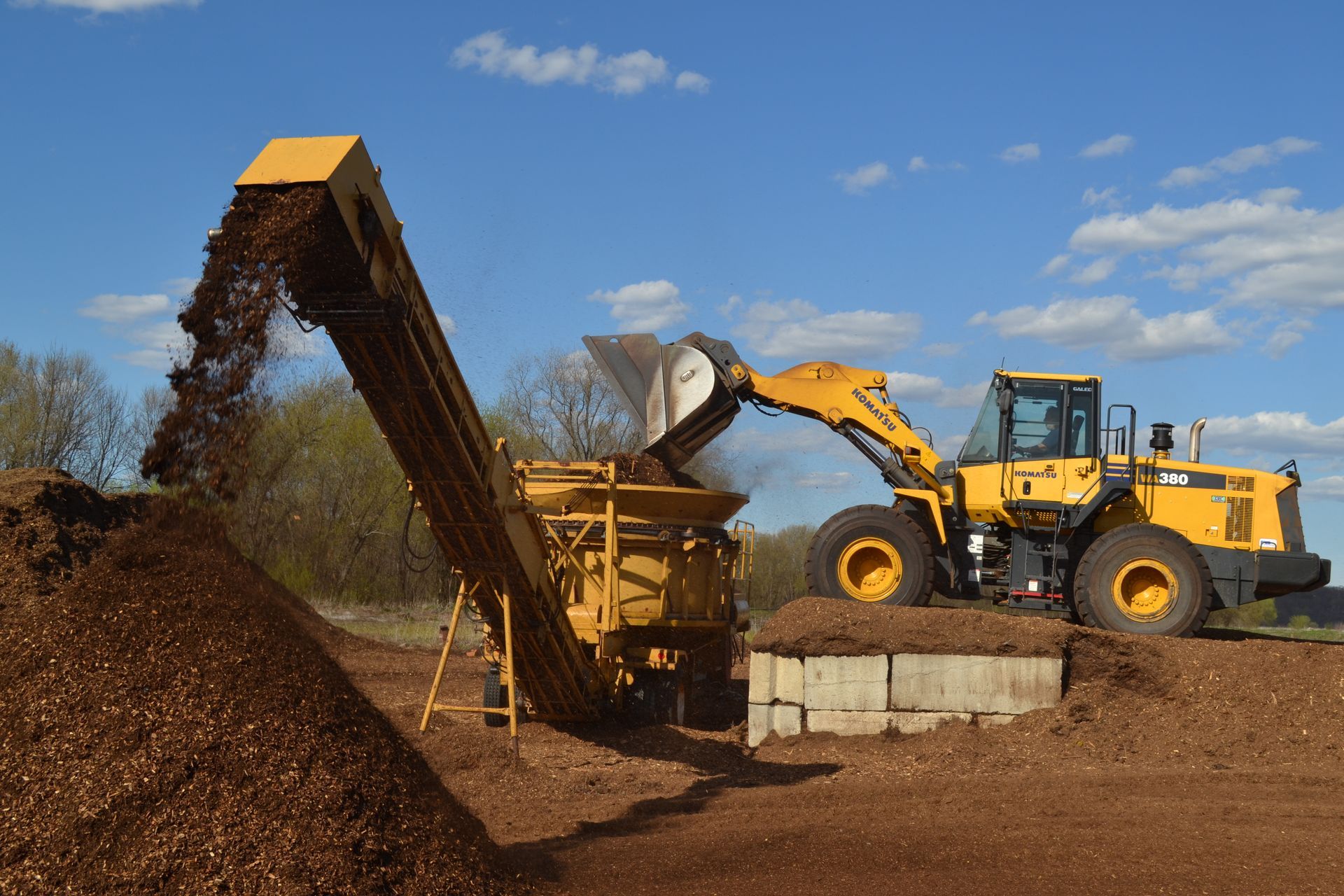 a yellow tractor is loading a pile of dirt into a conveyor belt