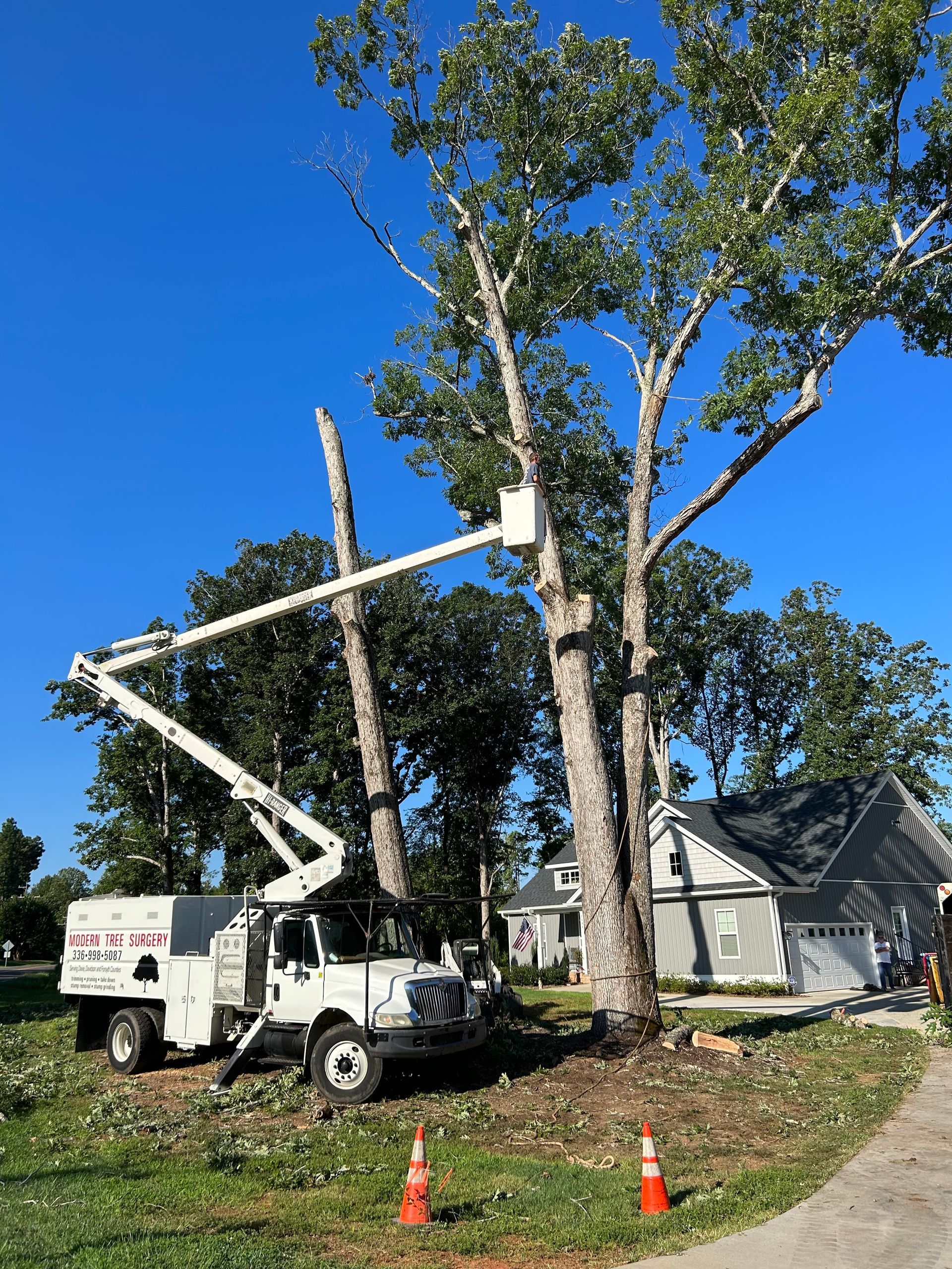 A white truck is cutting a tree in front of a house.