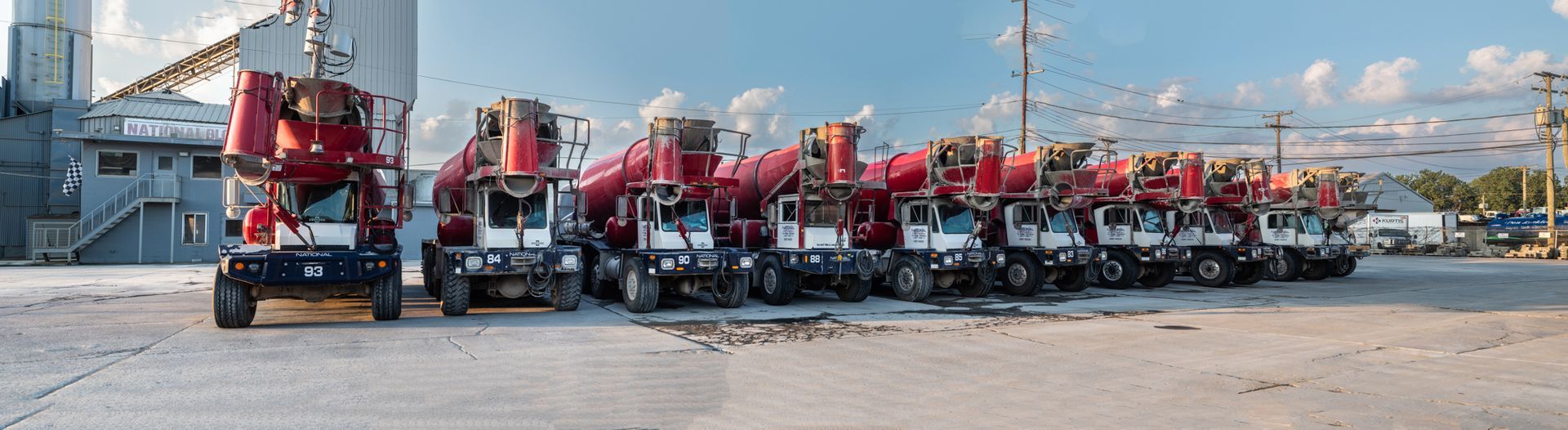 A row of concrete mixers are parked in a parking lot.