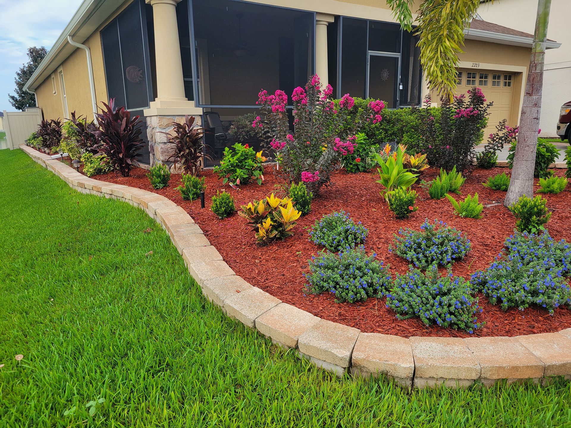 Front yard landscaping with red mulch and brick plant bed