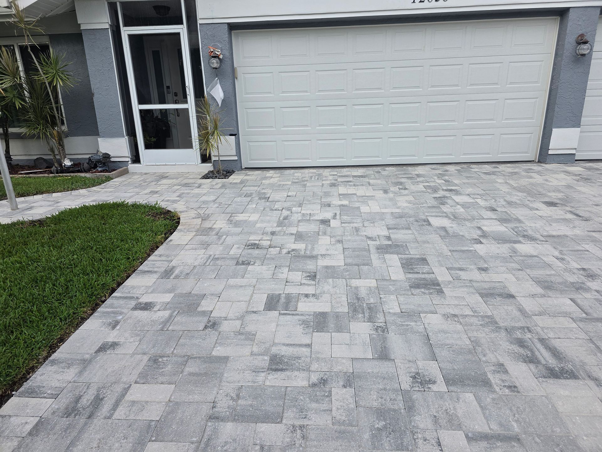 Gray paver driveway leading to a white garage door 