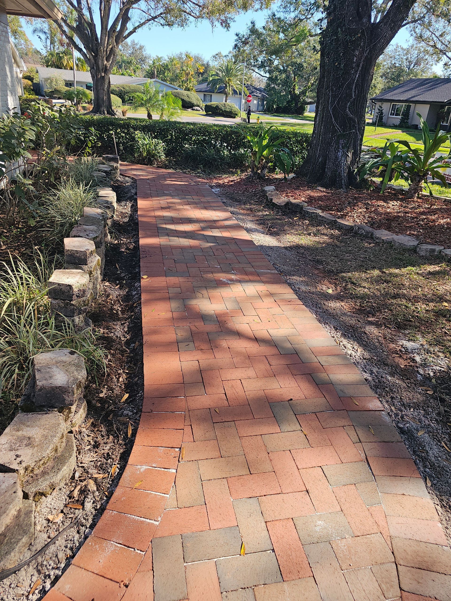 Brick garden path bordered by hedges and trees in a sunny outdoor park-like setting