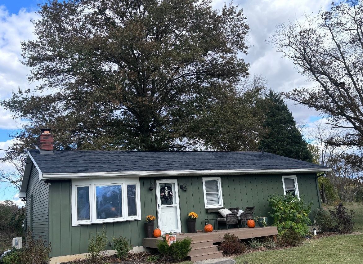 A green house with a black roof and pumpkins on the porch.