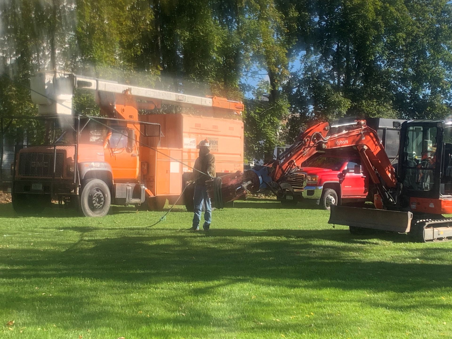 Orange tree trimming truck and excavator on a grassy field with a worker in front.