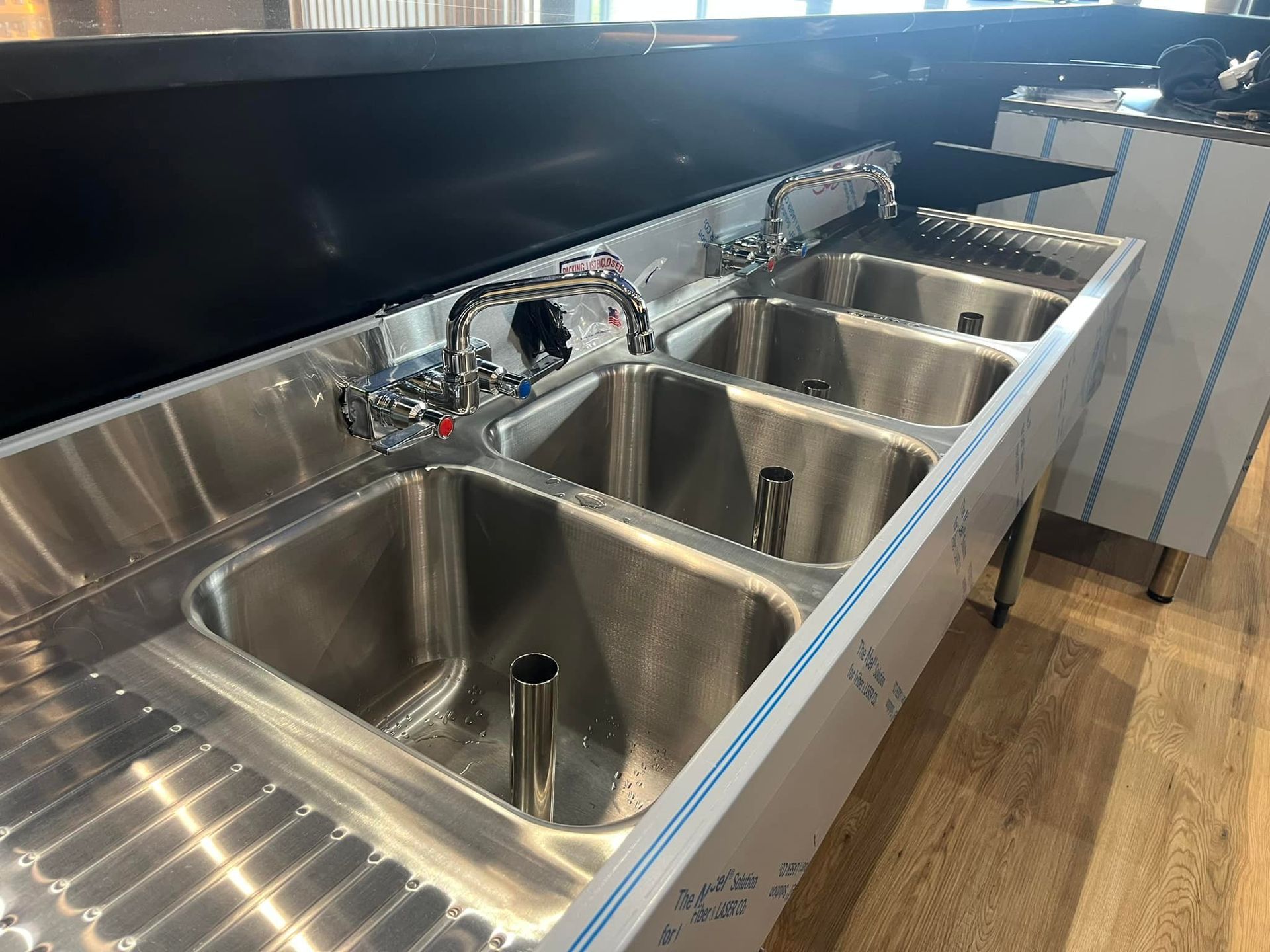 Stainless steel commercial sink with multiple basins and faucets.