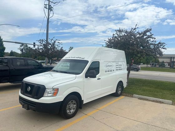 White Nissan NV van parked outside, with commercial lettering on side, in a parking lot.