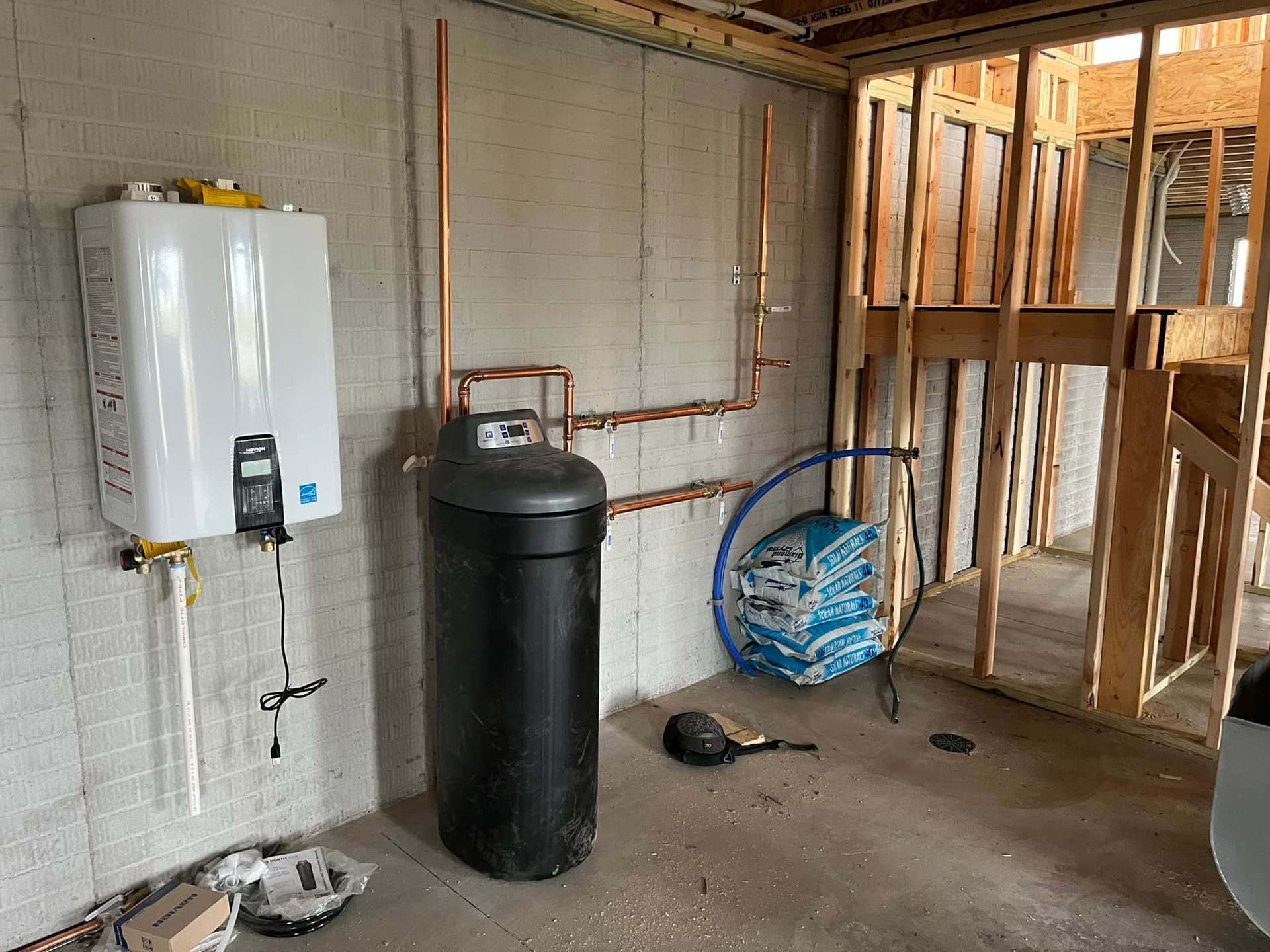Water heater and water softener in unfinished basement with copper pipes and framing.
