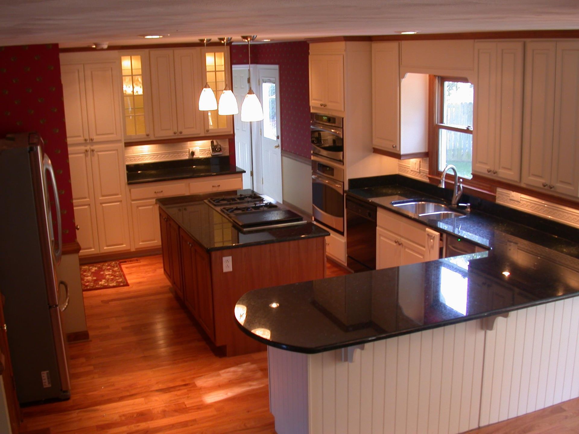 Modern kitchen with cream cabinets, black countertops, wood island, and dark red wall.