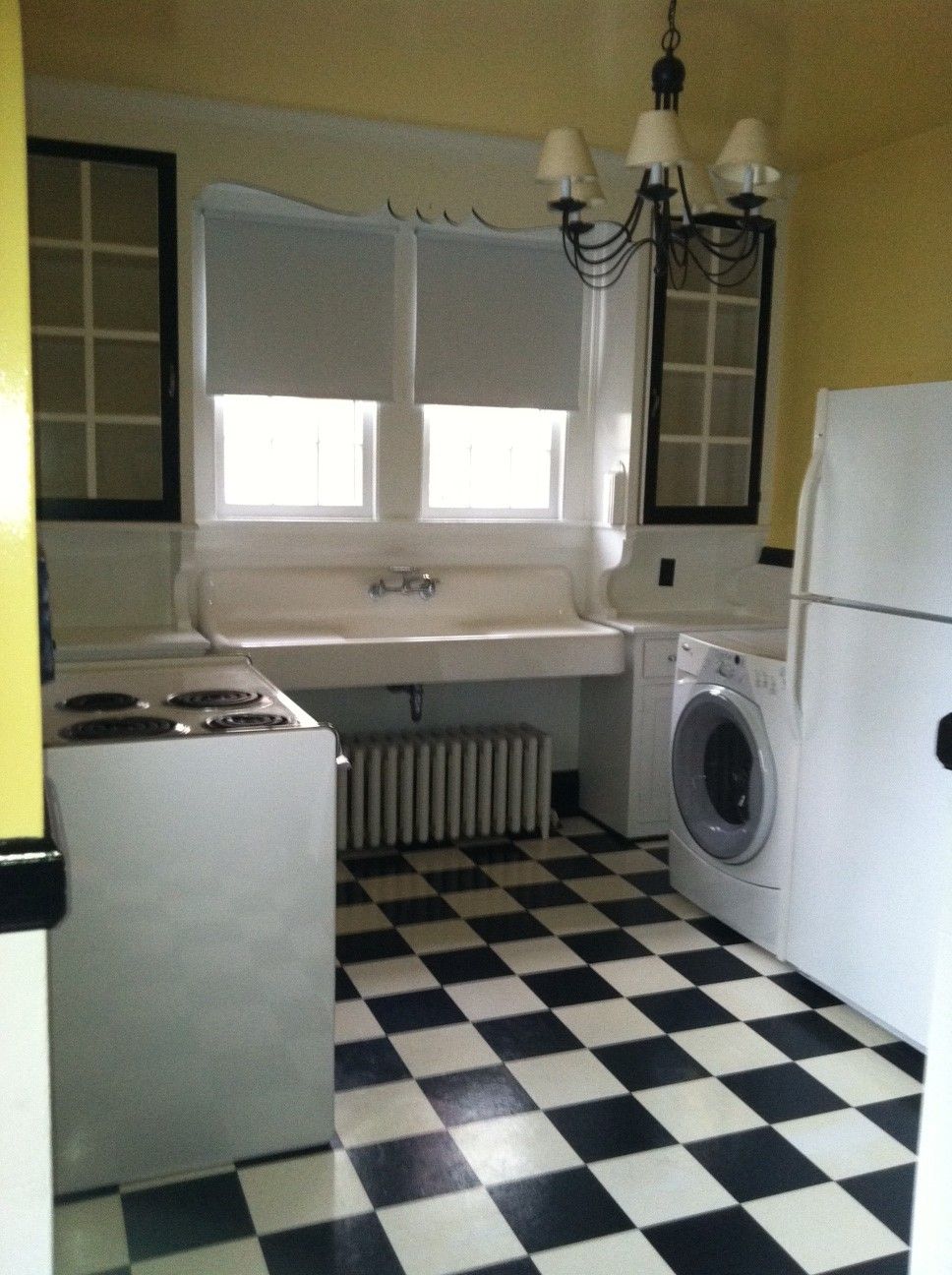 Black and white tiled kitchen with appliances, sink, and cabinets. Yellow walls and a window.