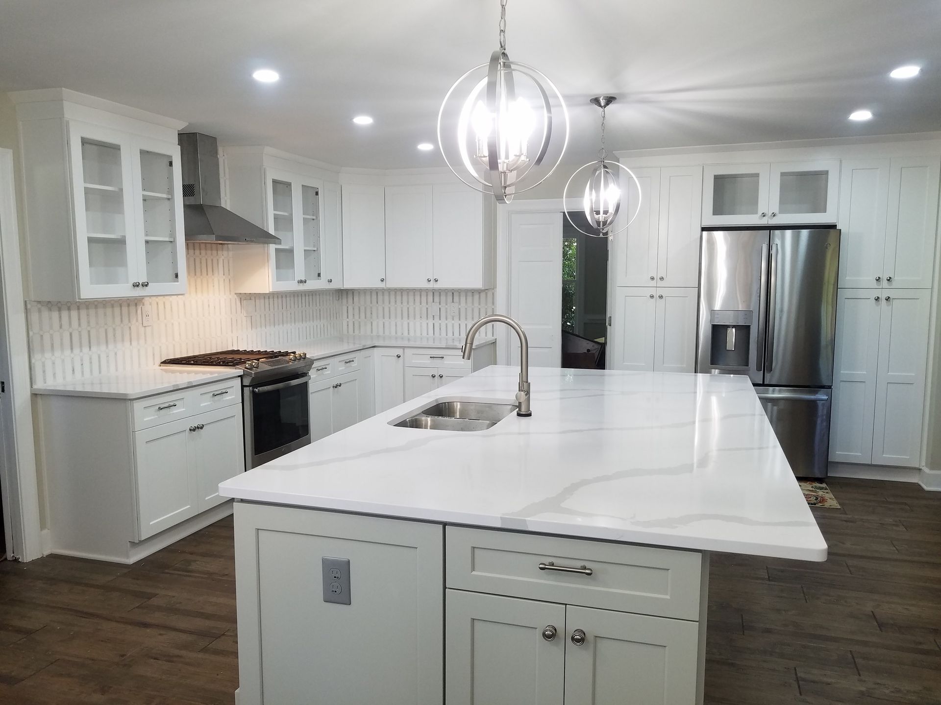 White kitchen with large island, stainless steel appliances, and globe pendant lights.