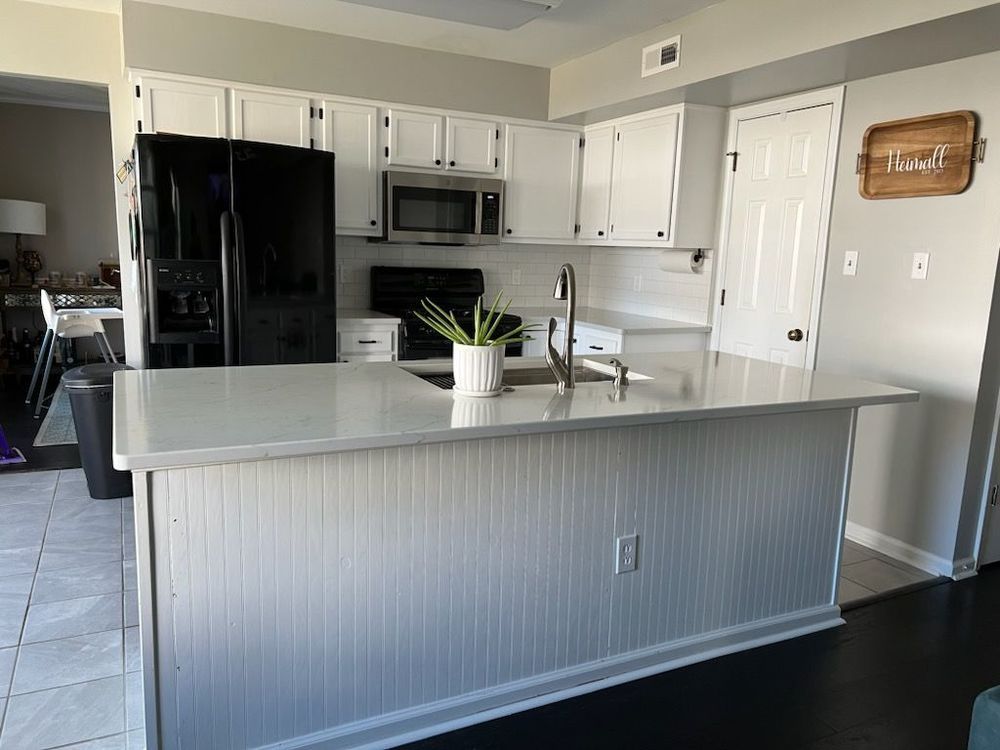 White kitchen with black appliances, a beadboard island, and a light countertop.