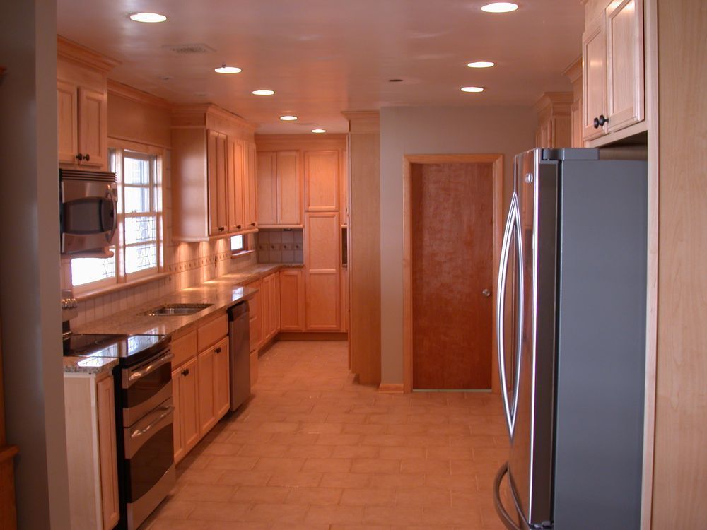 A light wood kitchen with stainless steel appliances, cabinets, and a closed brown door.