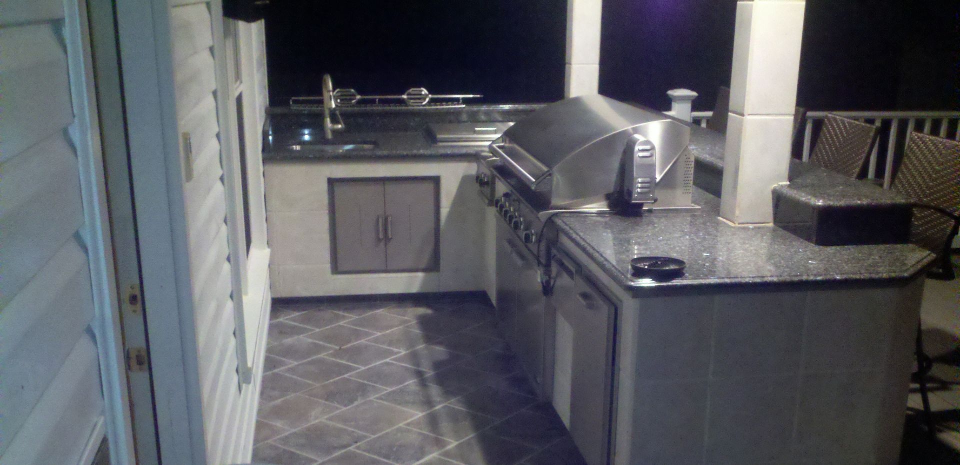 Outdoor kitchen with grill, countertop, cabinets, and a rotisserie grill. Nighttime setting.