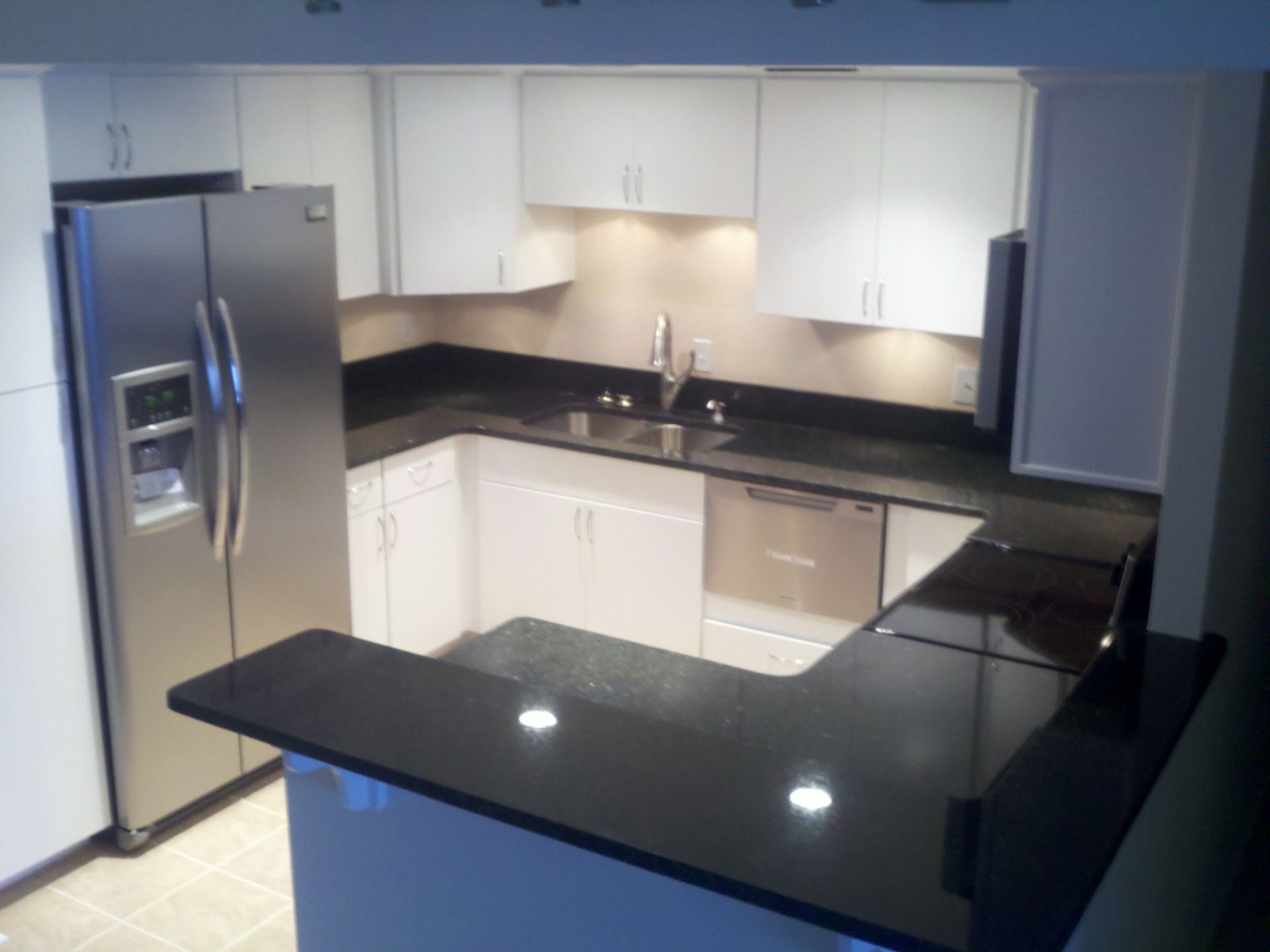 Stainless steel appliances in a bright kitchen with white cabinets, black countertops, and a breakfast bar.
