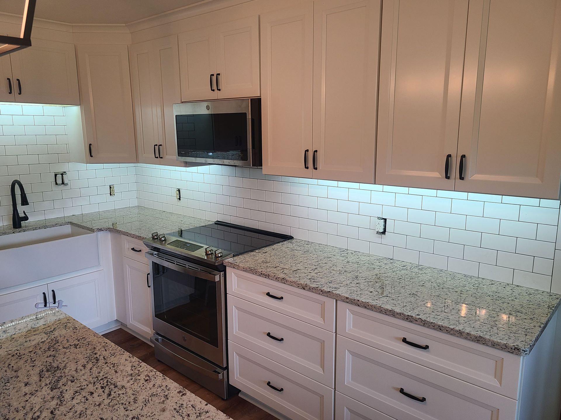 White kitchen with granite countertops, stainless steel appliances, and tile backsplash.