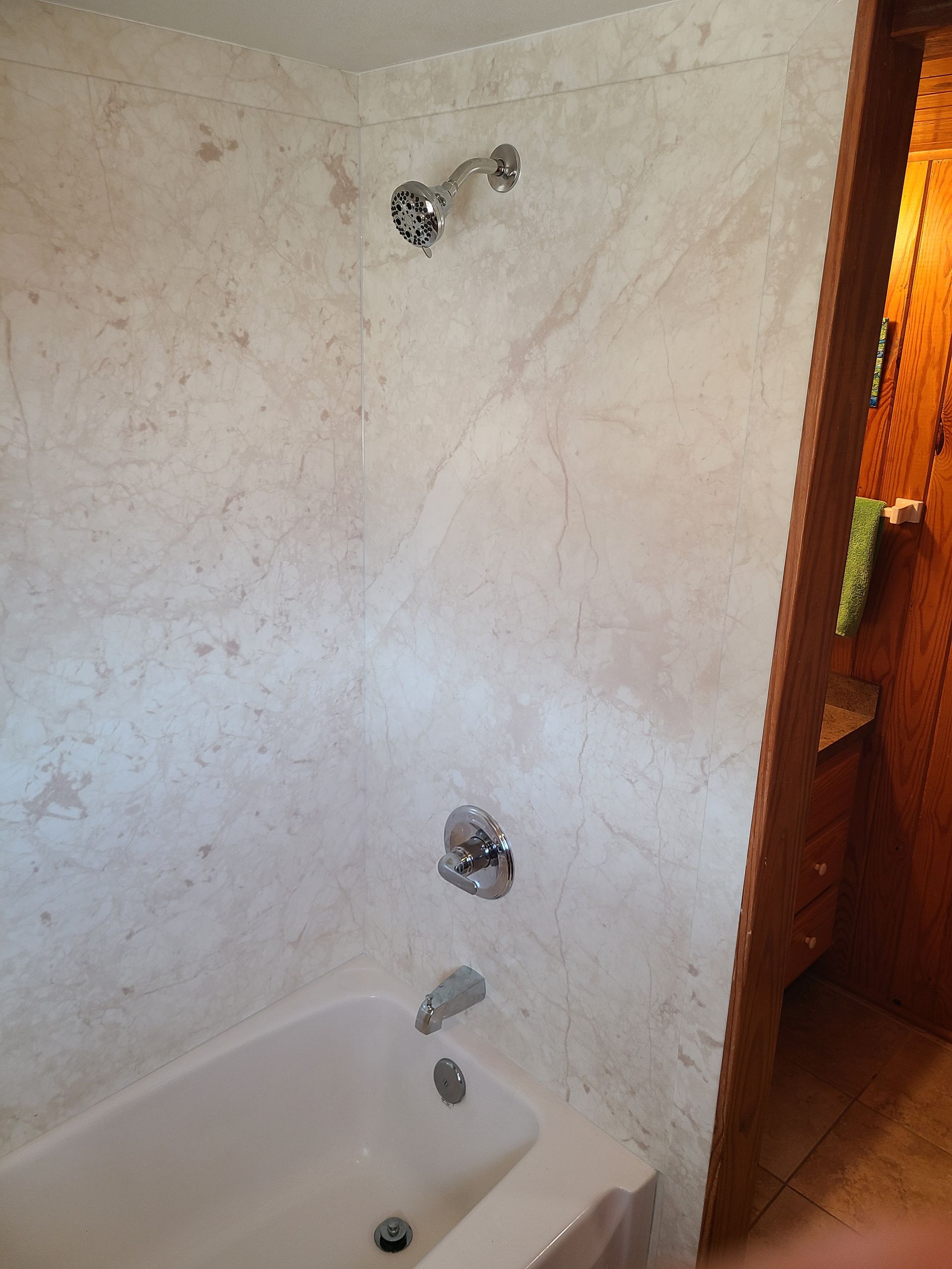 Shower with off-white marble-like walls, chrome fixtures, and a white tub. The bathroom door is partially visible.