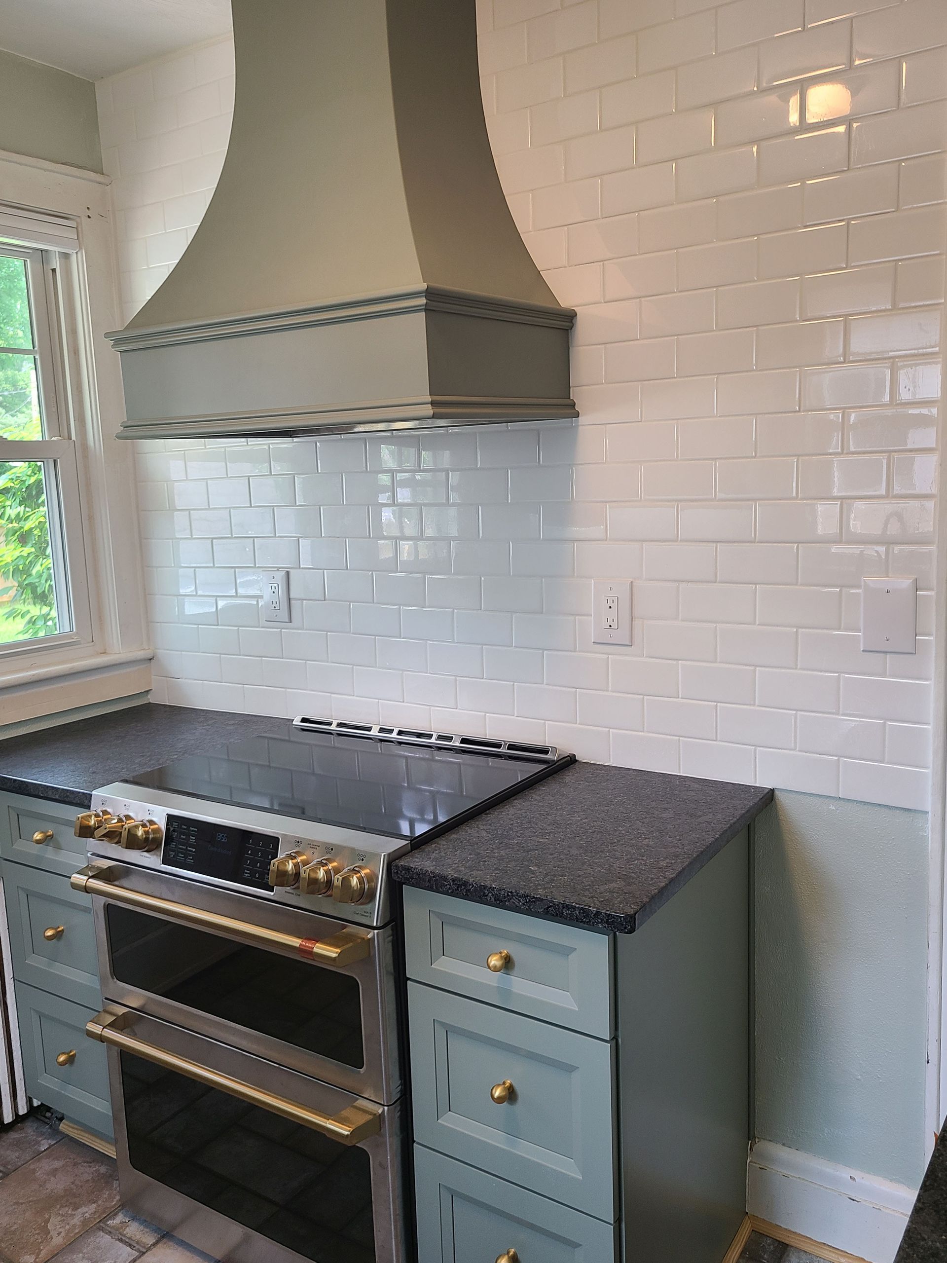 Kitchen with blue cabinets, white subway tile backsplash, and grey range hood.