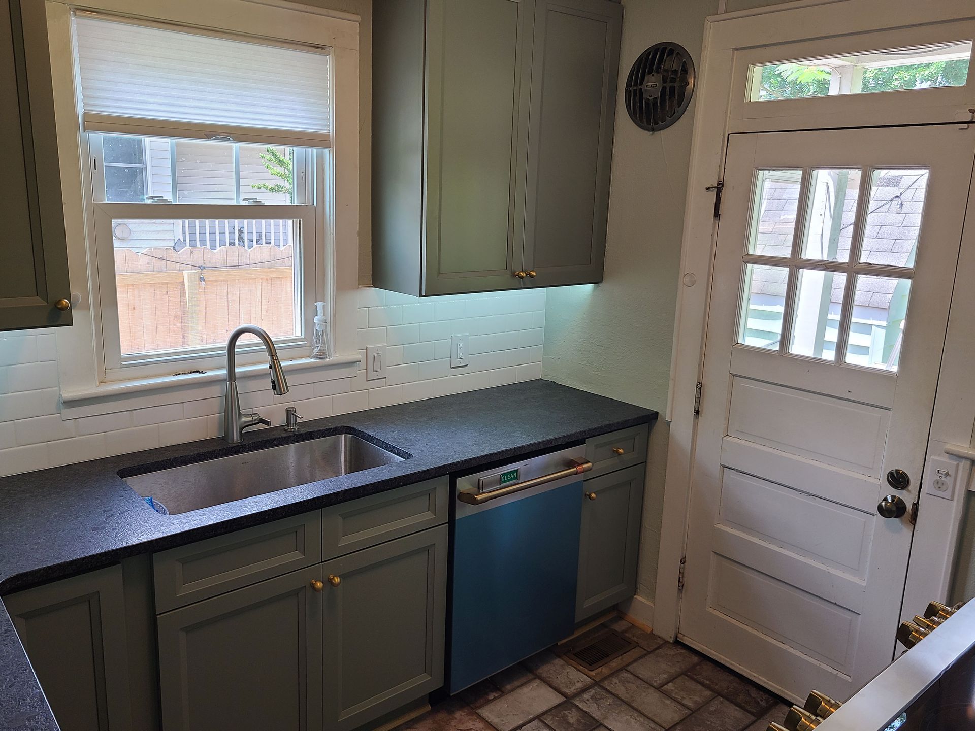 Kitchen with green cabinets, black countertop, stainless steel sink, and a back door.