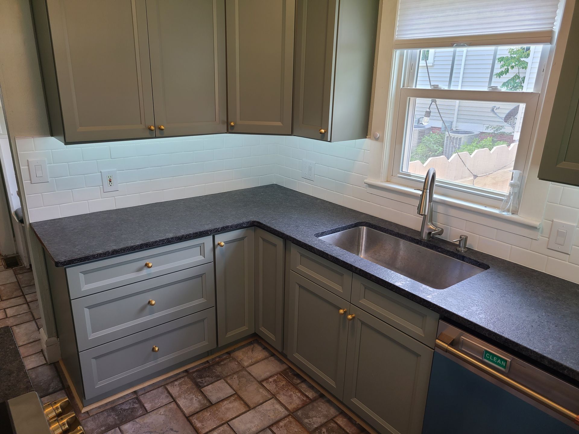 Kitchen corner with gray cabinets, dark countertop, stainless steel sink, and window.