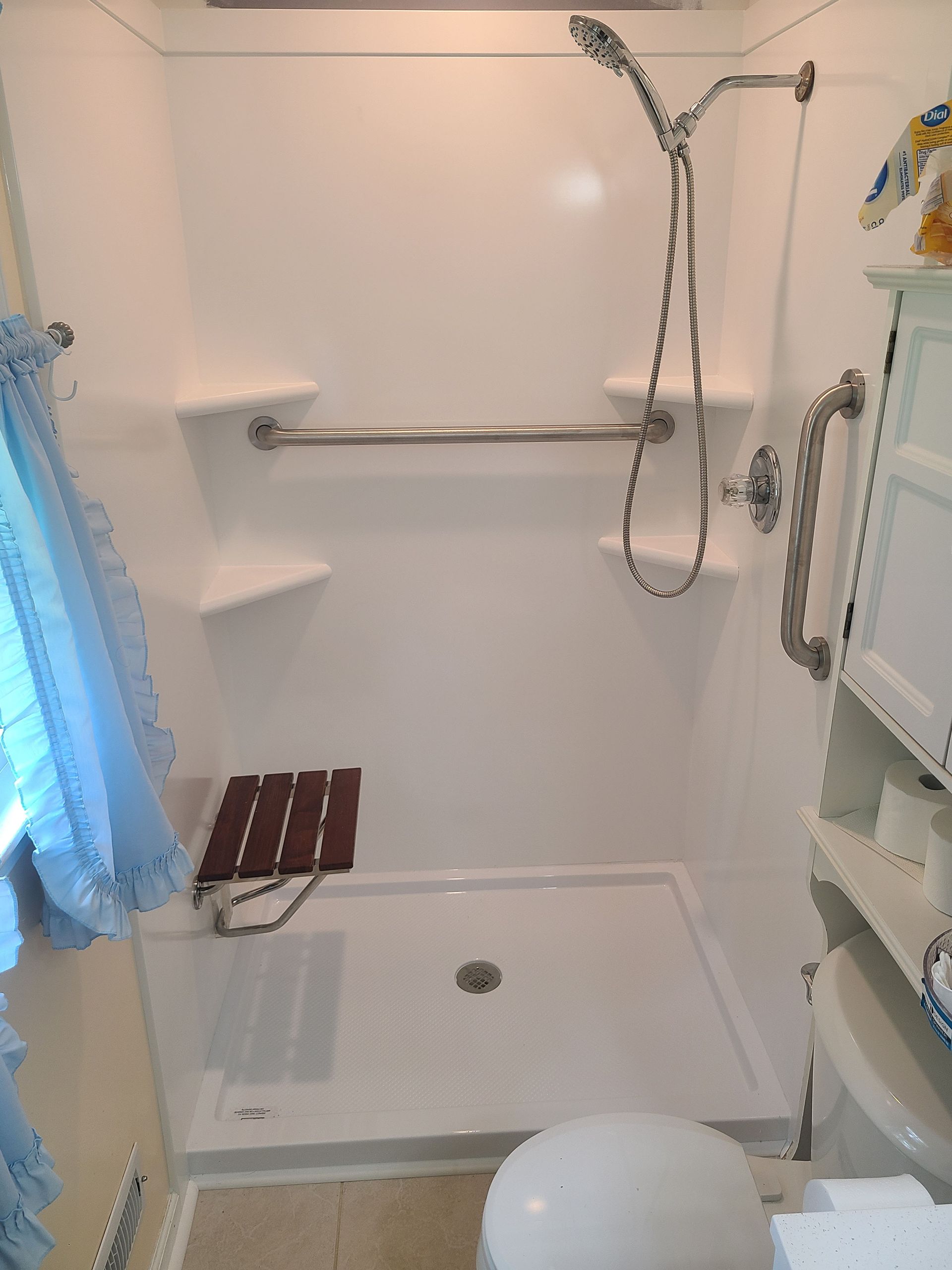 White accessible shower with grab bars, a seat, and a handheld showerhead; next to a toilet.