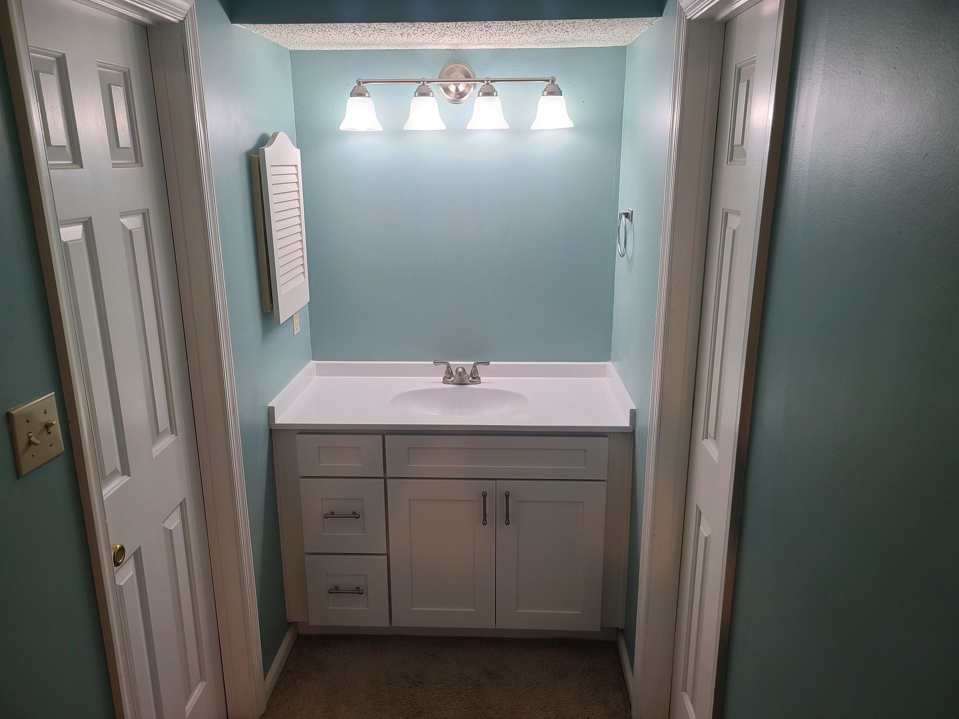 Bathroom with white vanity, turquoise walls, and two white doors.