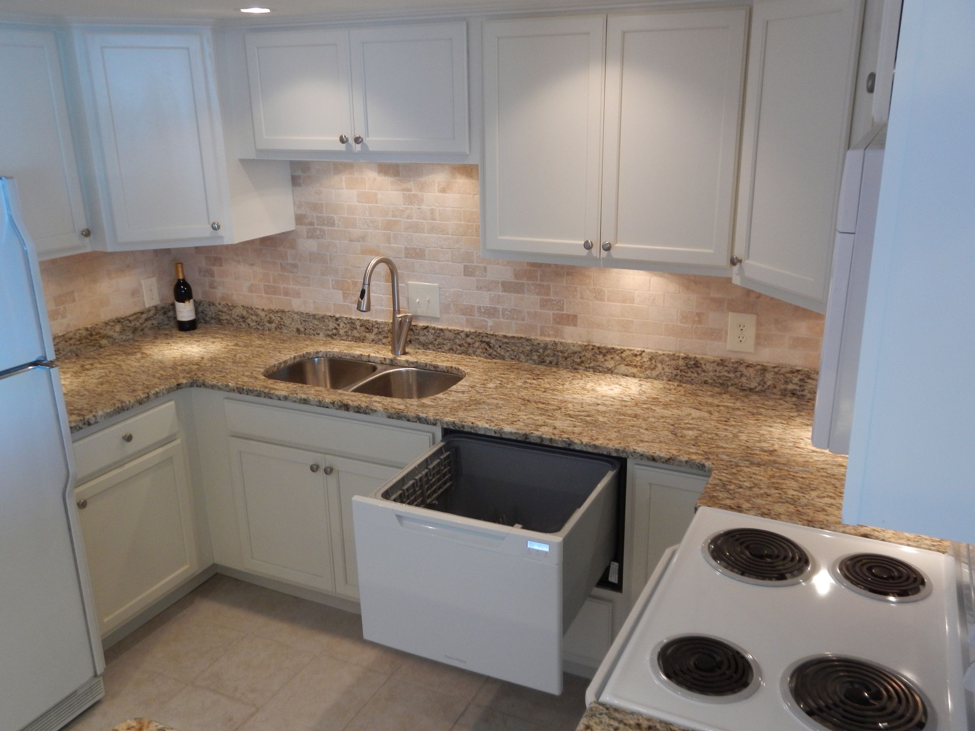 Small kitchen with white cabinets, granite countertops, and a pull-out trash bin.