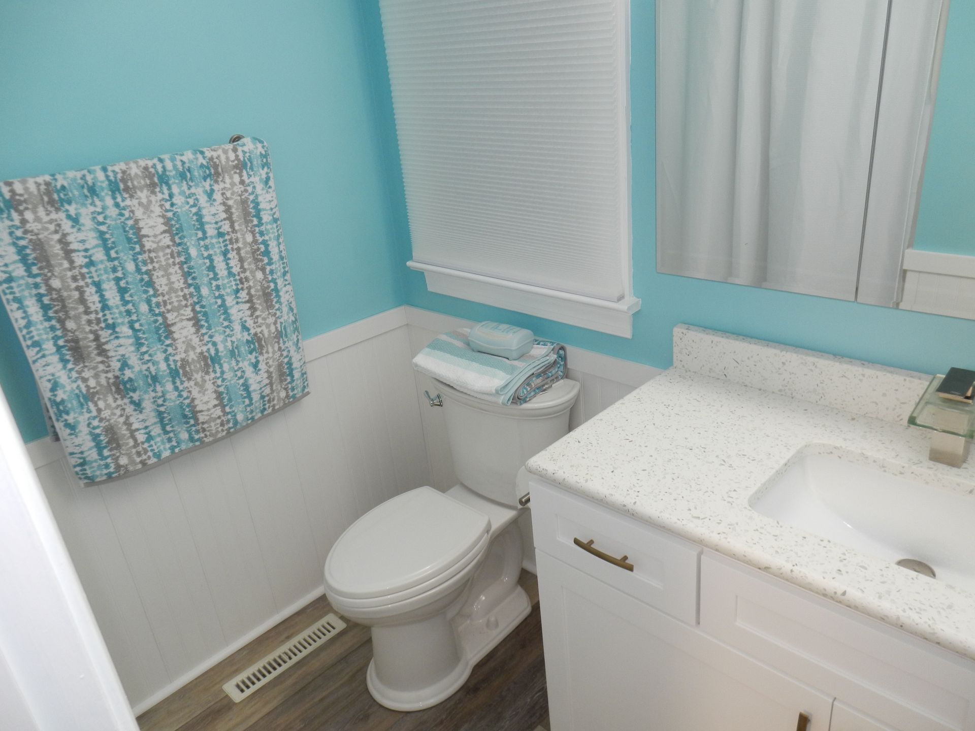 Bathroom with teal walls, white wainscoting, toilet, vanity, and towel hanging on the wall.