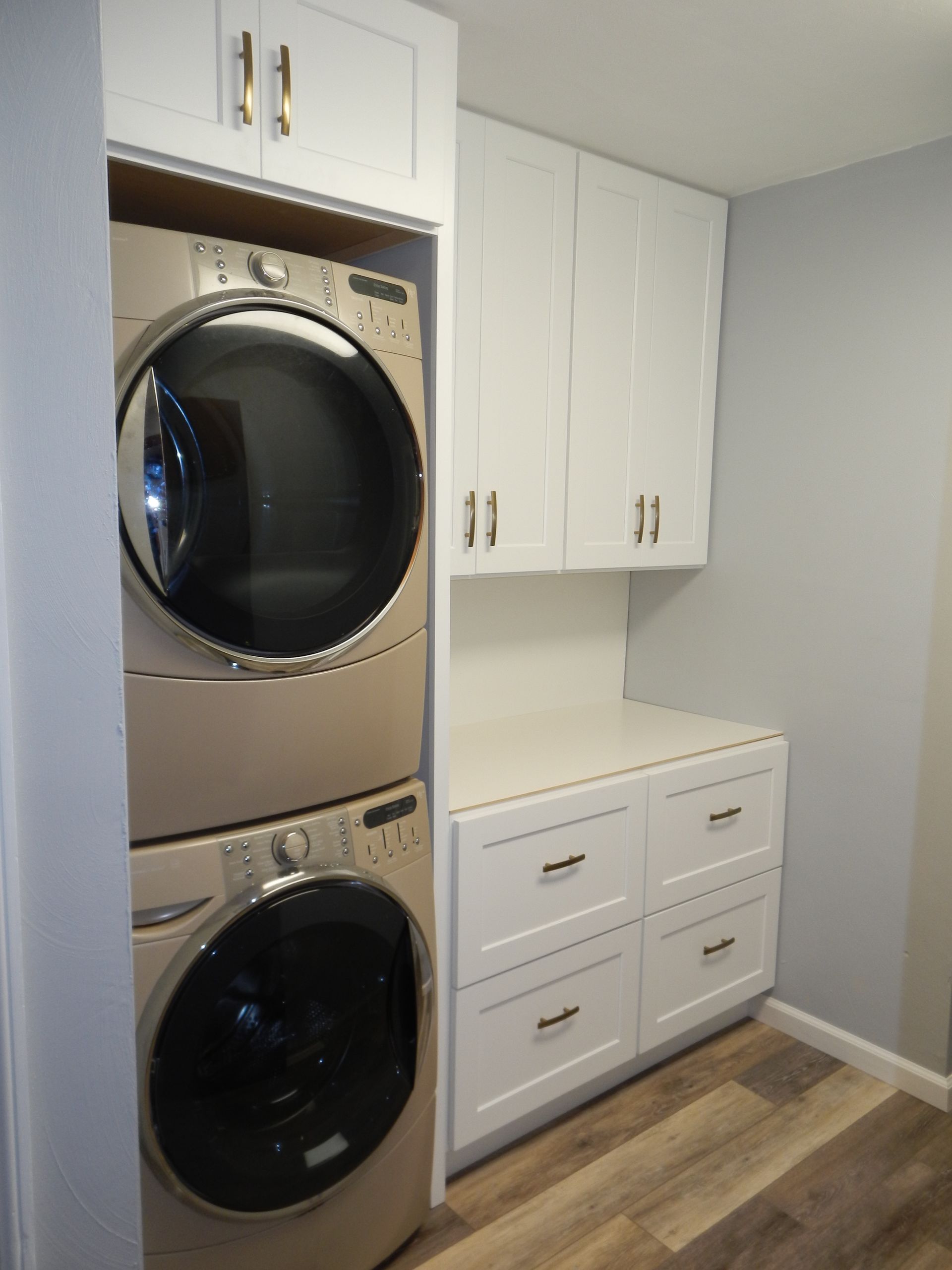 Laundry room with stacked washer and dryer, white cabinets, and drawers. Light wood-look flooring.