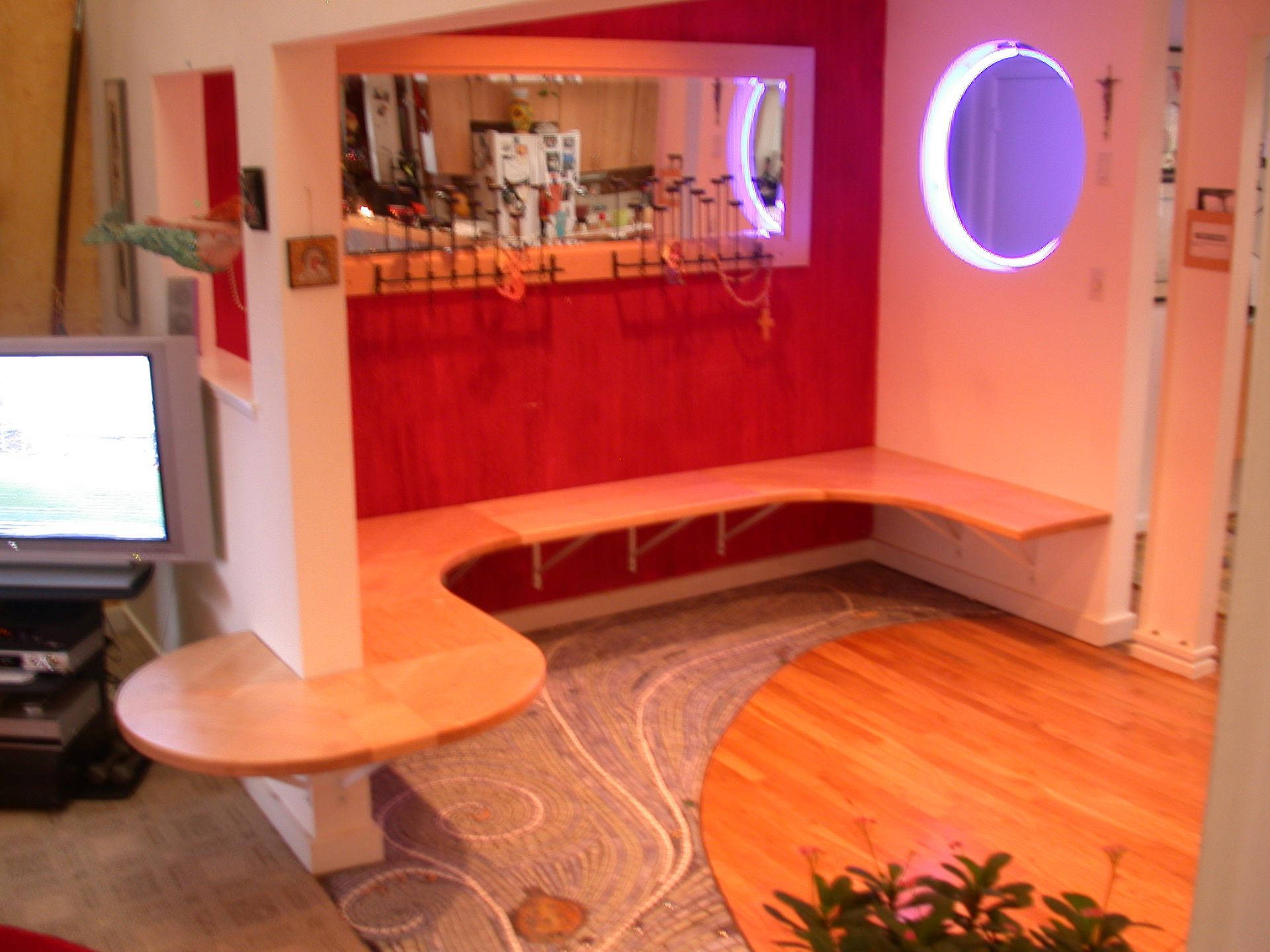 A unique, red-walled, curved booth with a bench seat and bar area with a round window.