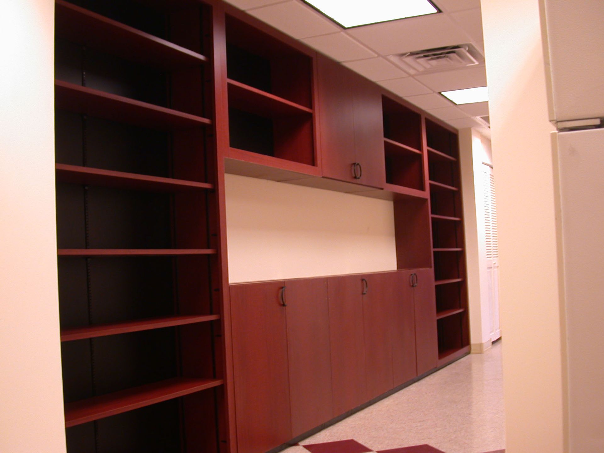 Built-in dark red cabinetry with shelves and storage in a hallway with beige walls and patterned floor.