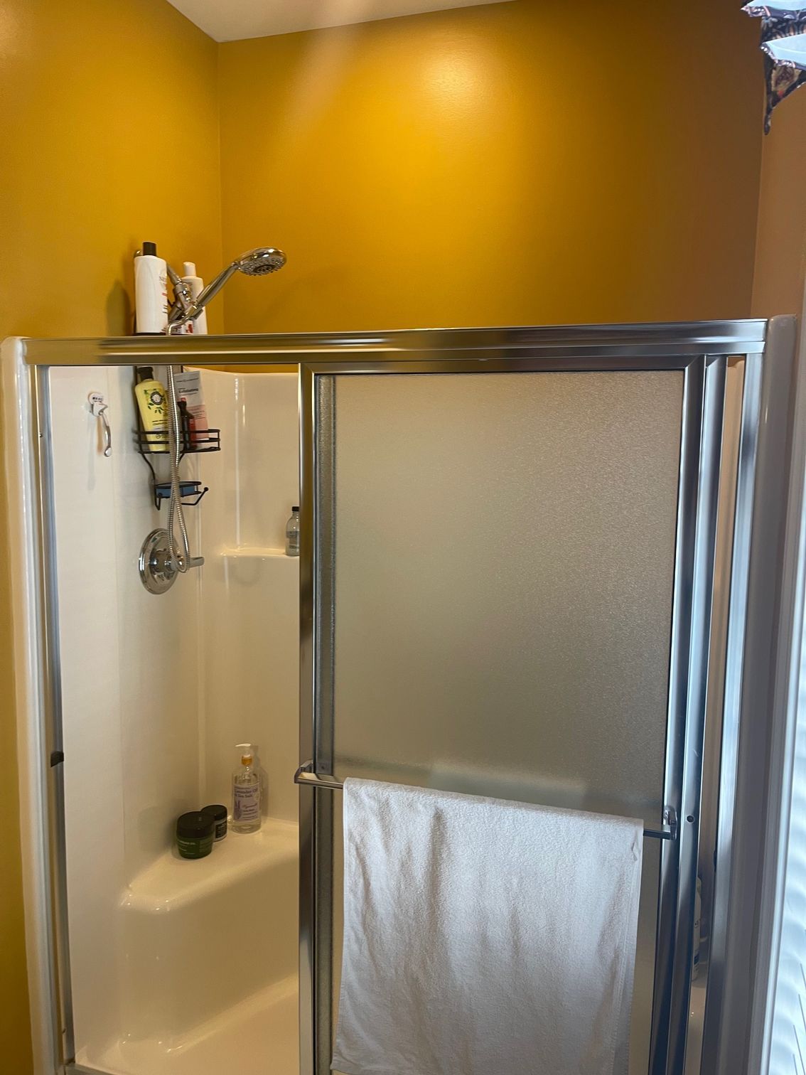 Shower with frosted glass doors, set in a yellow-walled bathroom. A towel hangs on the door.