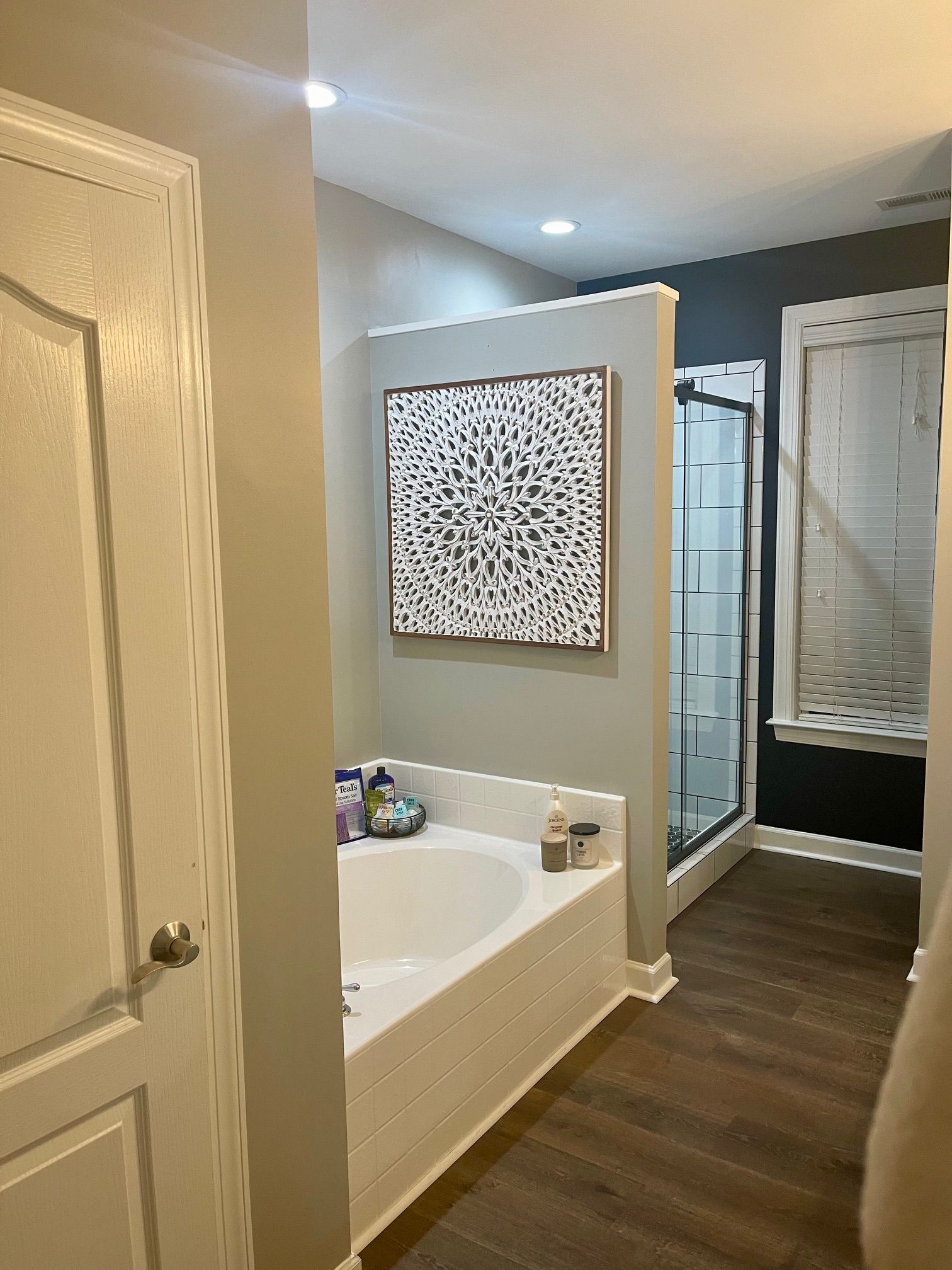 Bathroom with a bathtub, shower, and artwork. Gray and white walls with wood flooring.