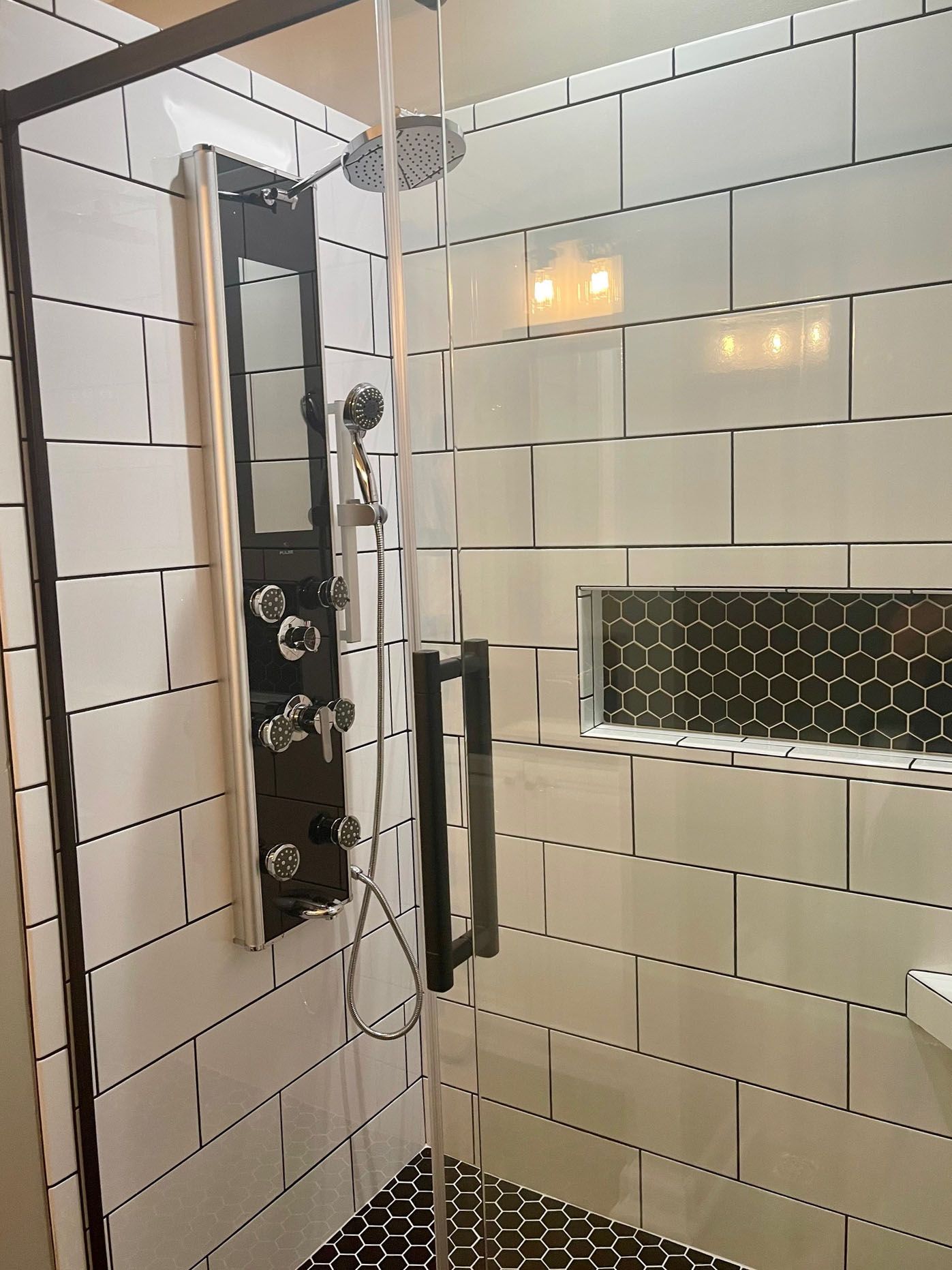 Modern shower with white subway tiles, black accents, and glass door.